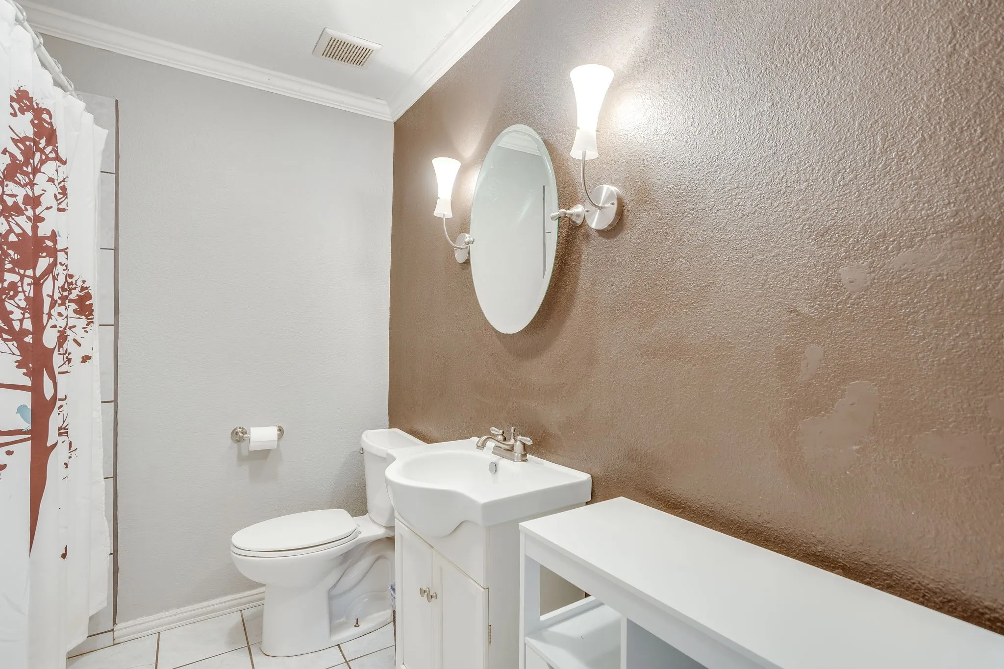 Elegant half bath featuring a pedestal sink with chrome fixtures, oval mirror with integrated sconce lighting, and textured taupe accent wall