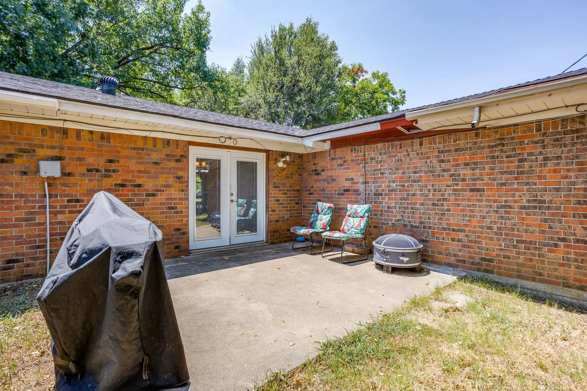 Exterior brick wall featuring a concrete patio and double glass-paneled doors