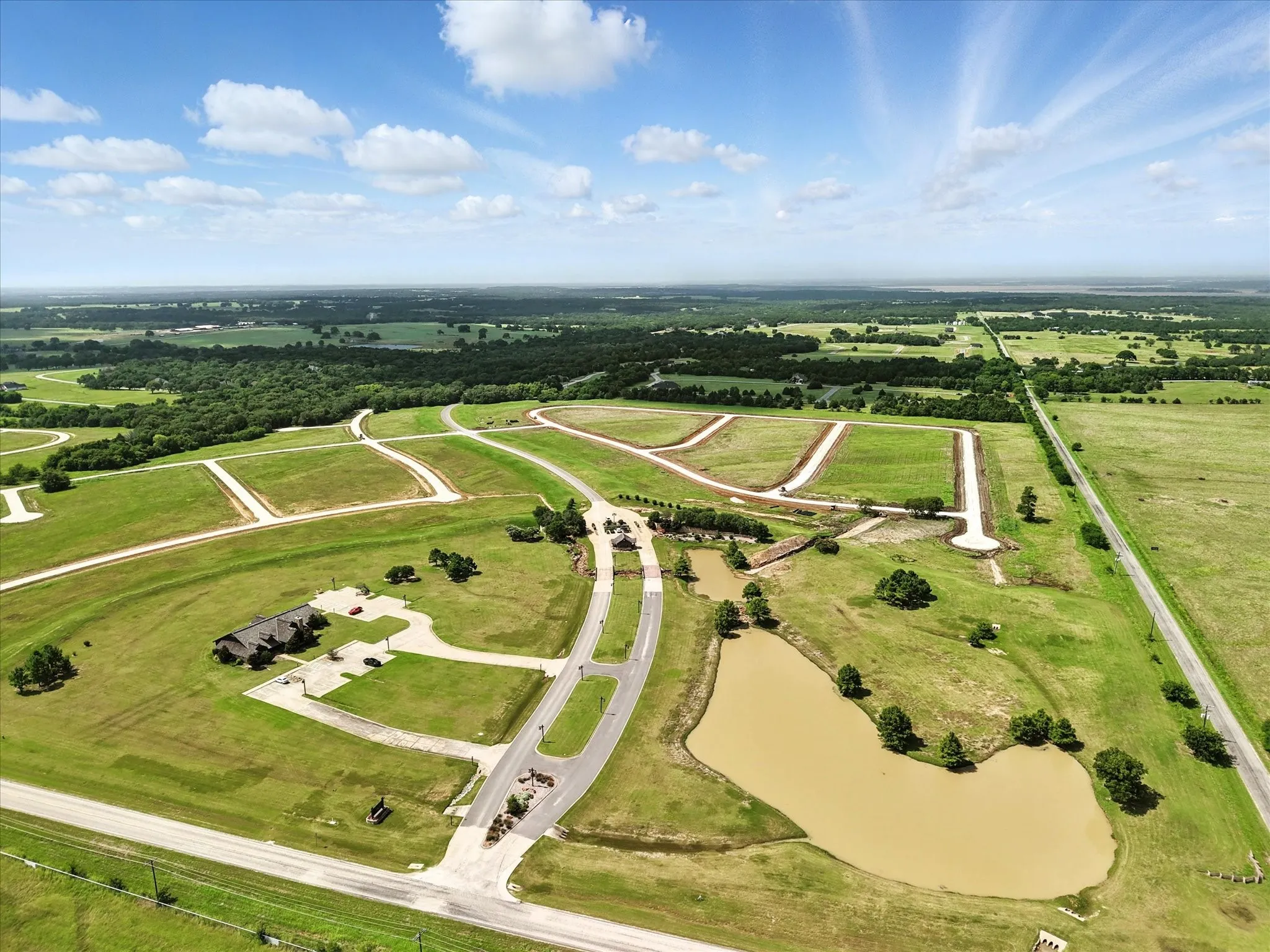 Aerial view showcasing a custom-designed residential community with extensive paved roadways, multiple buildable lots with mature trees, and a natural retention pond