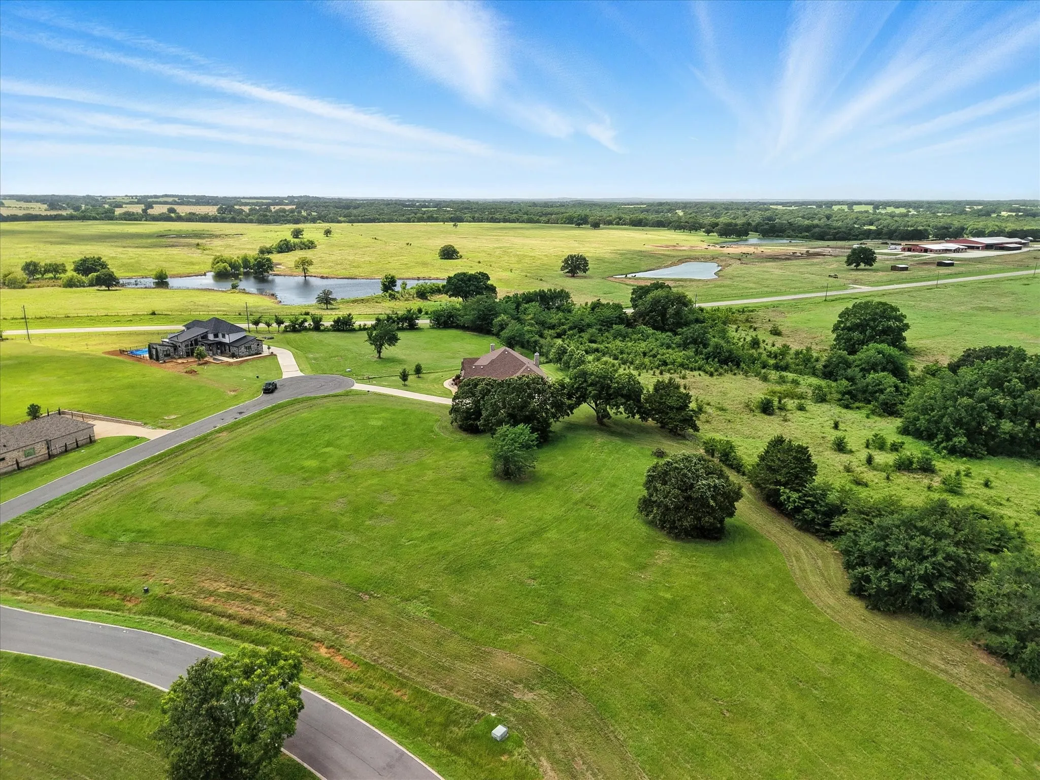 Expansive green landscape featuring multiple ponds, mature trees, and a dark-toned residence with a visible pool area