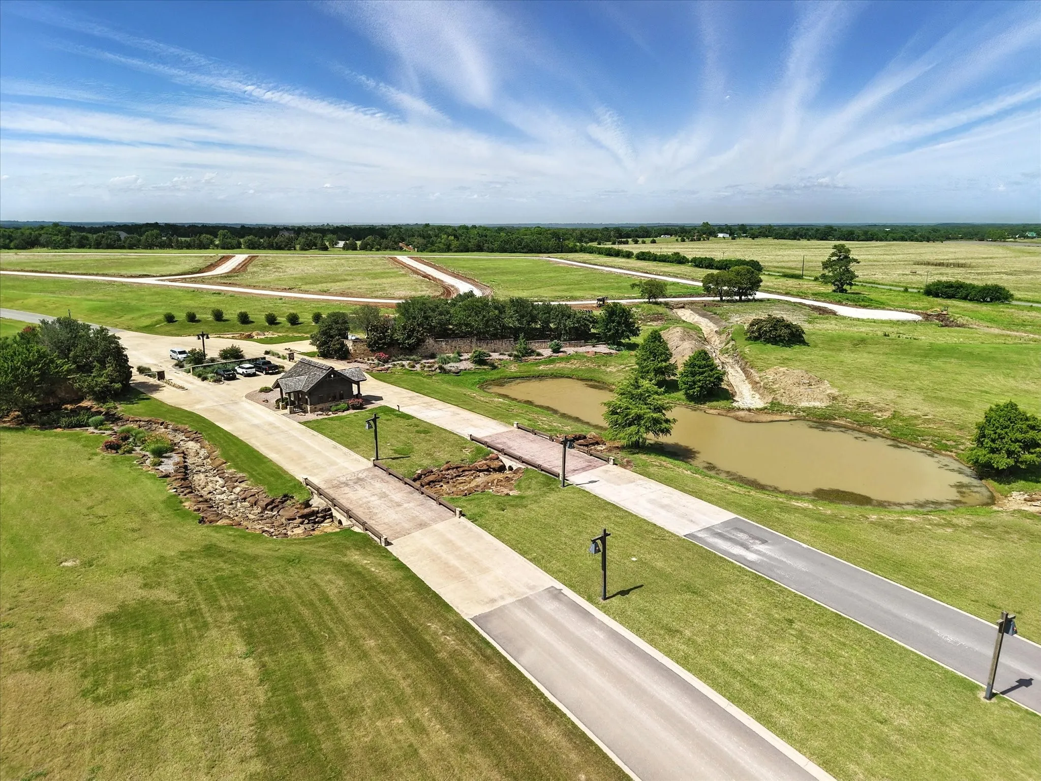 Expansive green landscape featuring newly paved roads, a central pavilion, and two distinct ponds