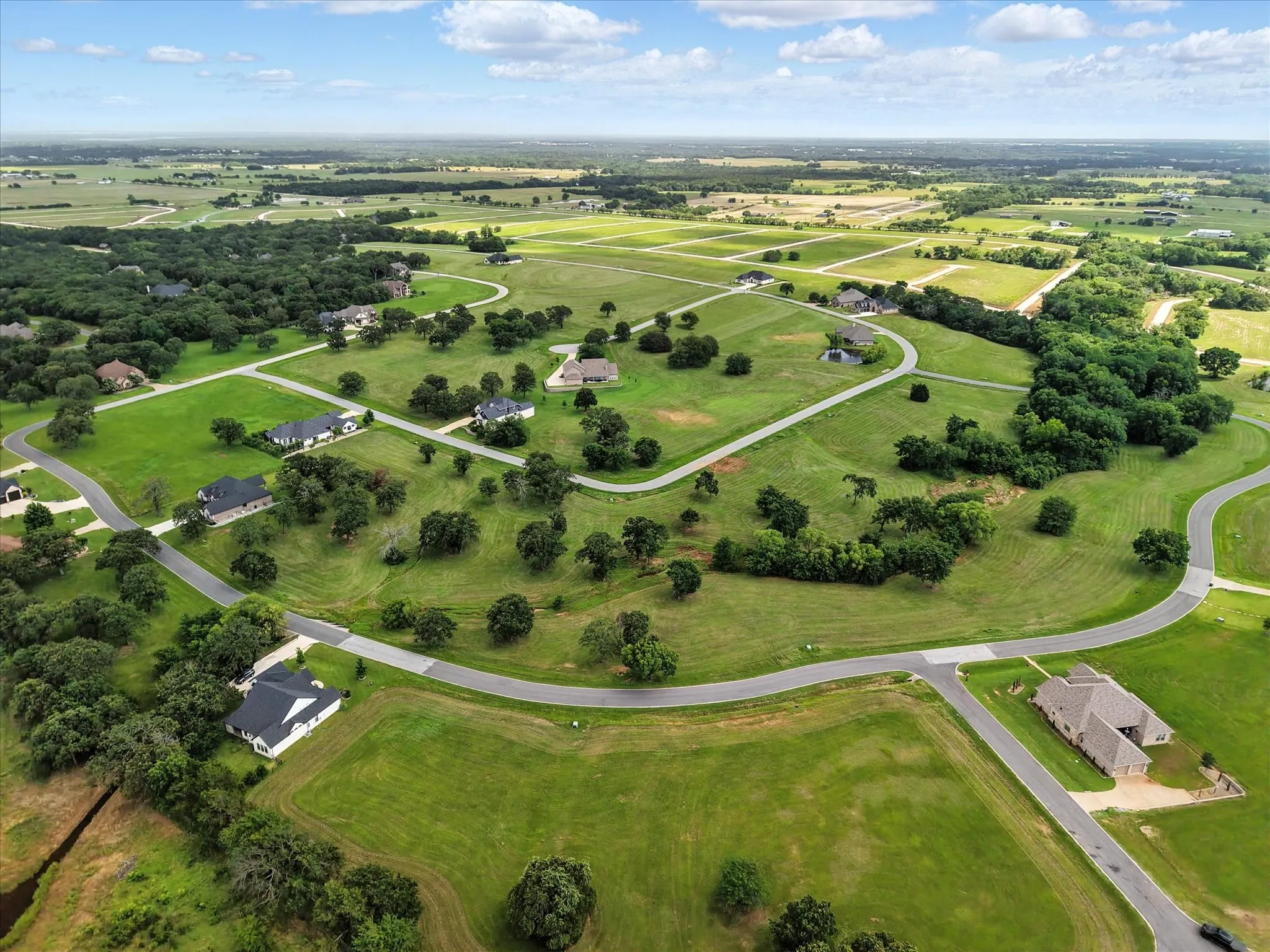 Expansive residential development featuring paved streets, mature trees, manicured green spaces, and distinct home sites