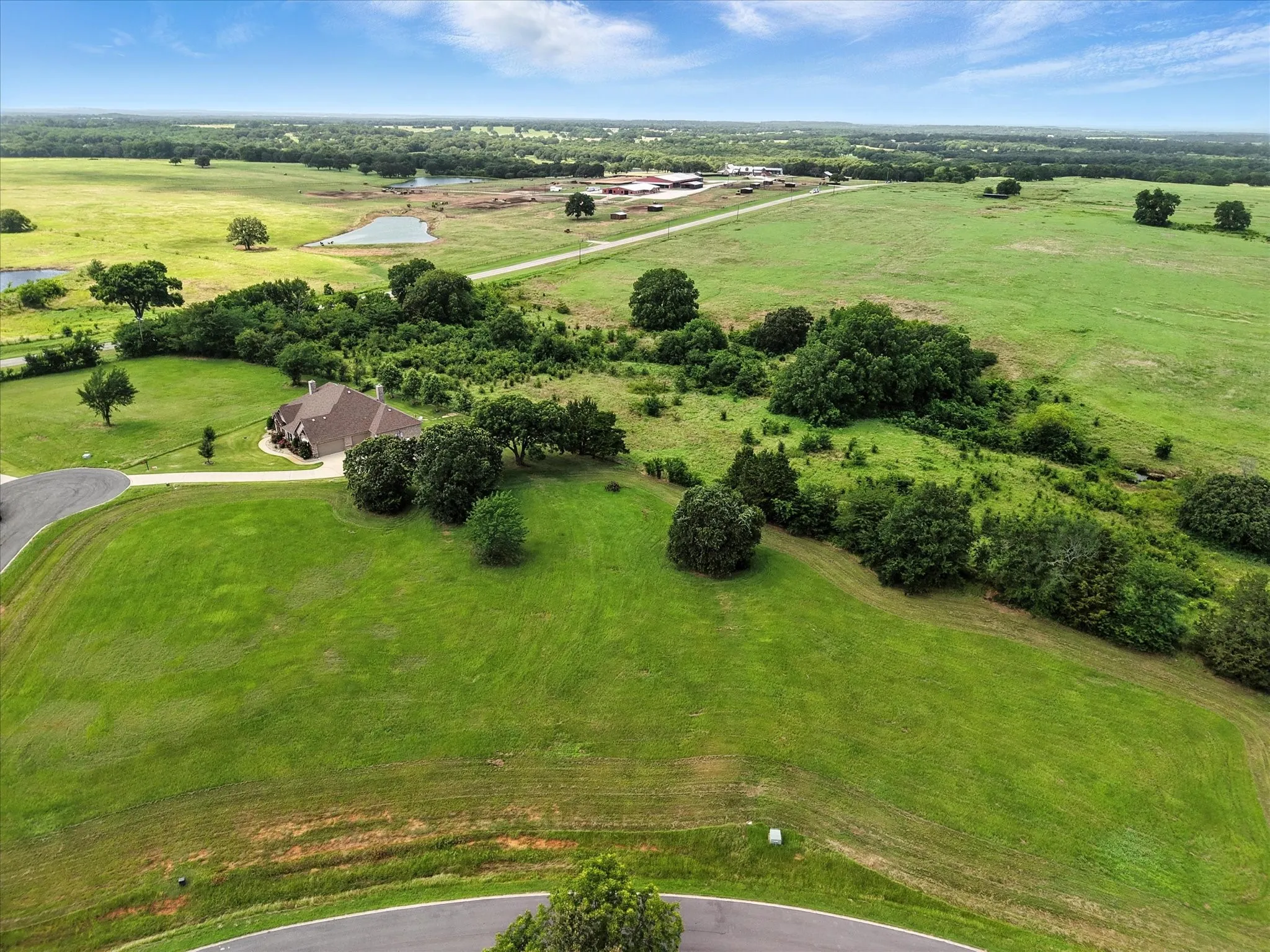 Sprawling rural estate showcasing lush pastureland with mature tree clusters, curved driveway access, and multiple outbuildings set across expansive acreage