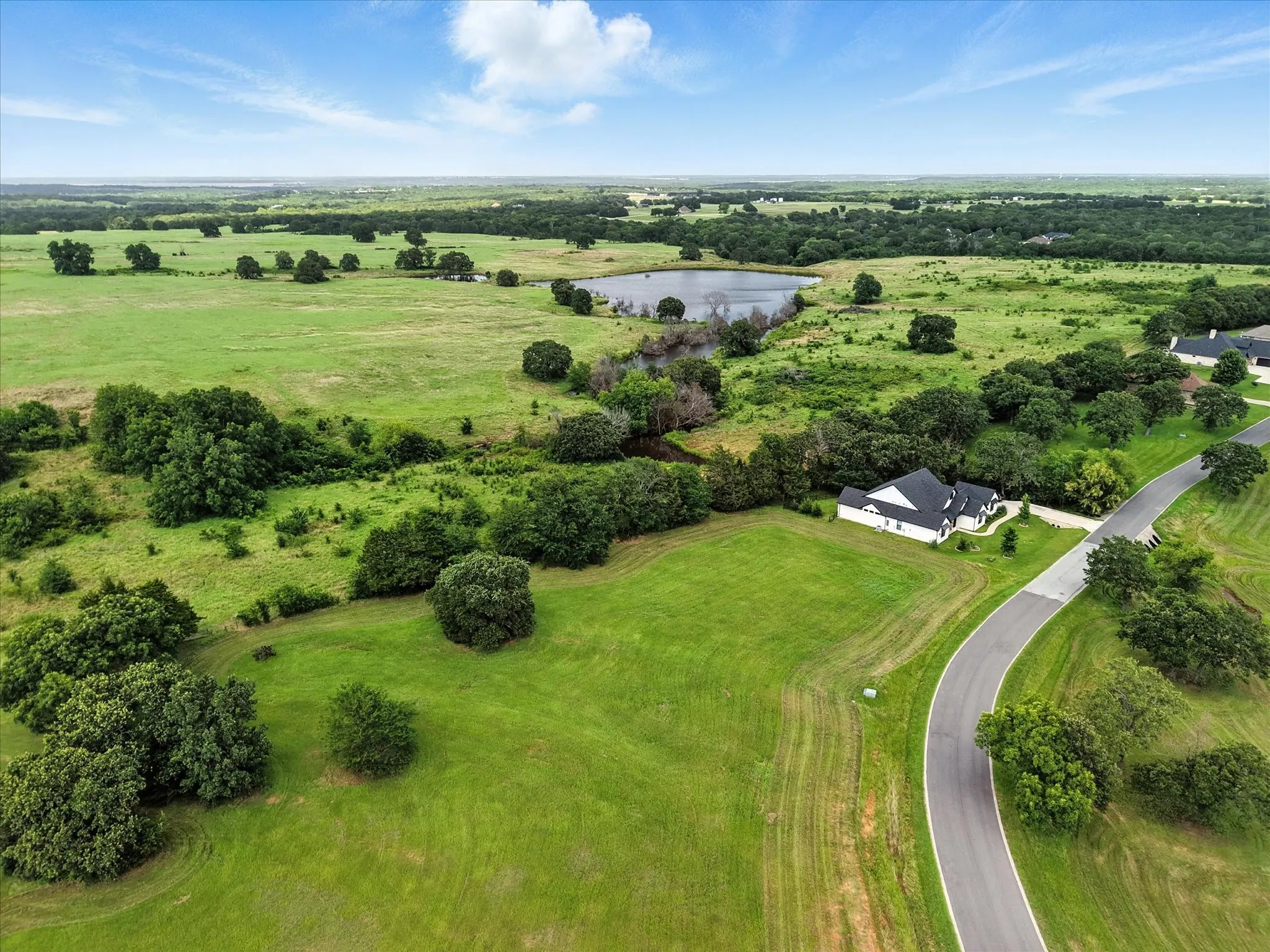 Picturesque rural estate set on expansive grounds featuring mature tree-lined property, a private pond, and a curved driveway approach