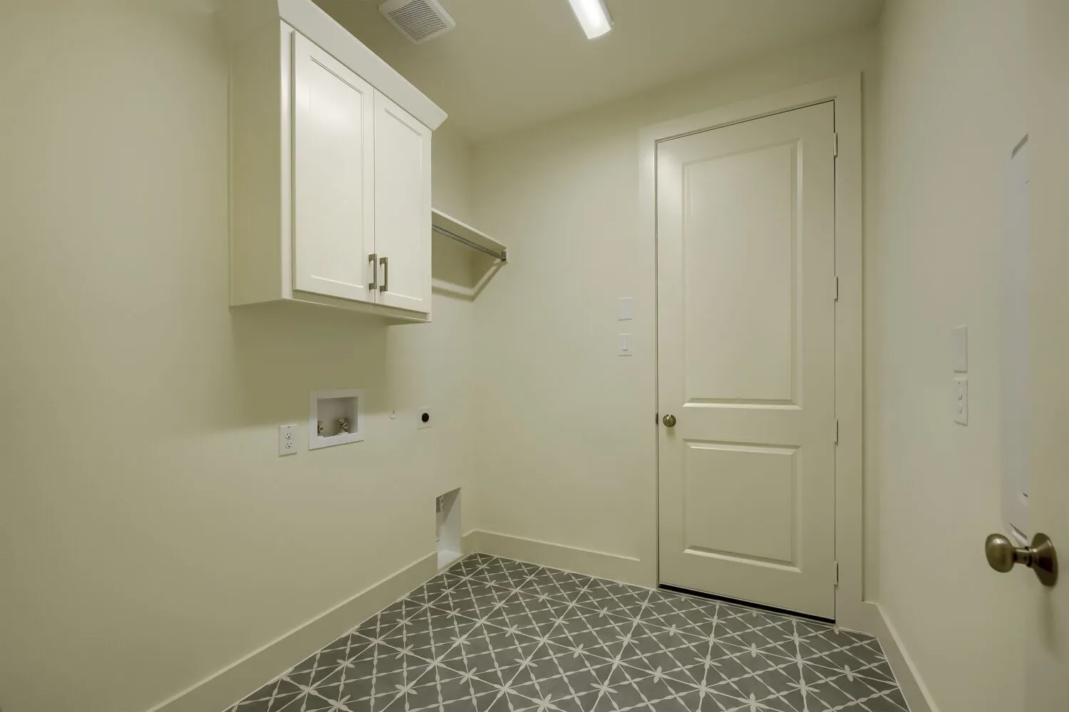 Laundry area featuring patterned floor tile, overhead cabinetry, and a clothes hanging rod
