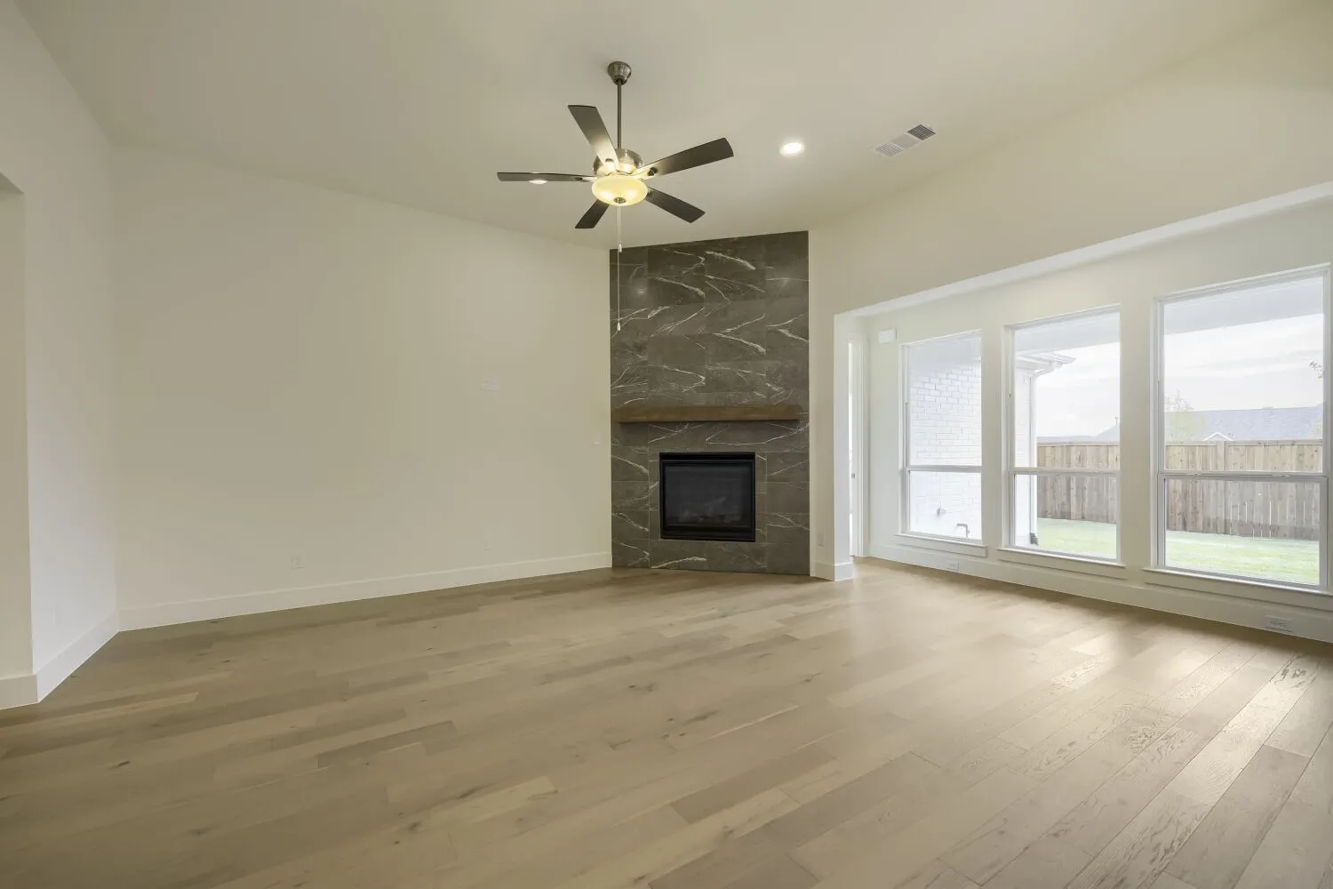 Vaulted ceiling featuring a ceiling fan, a fireplace with a stone-finish surround and wood-finish mantel, wood-finish flooring, and multiple windows