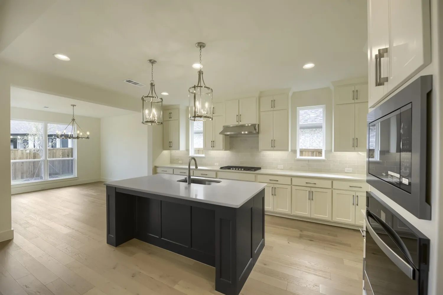 Open-concept kitchen featuring a dark-toned island with a light countertop, white cabinetry, integrated stainless steel appliances, and wood-finish flooring
