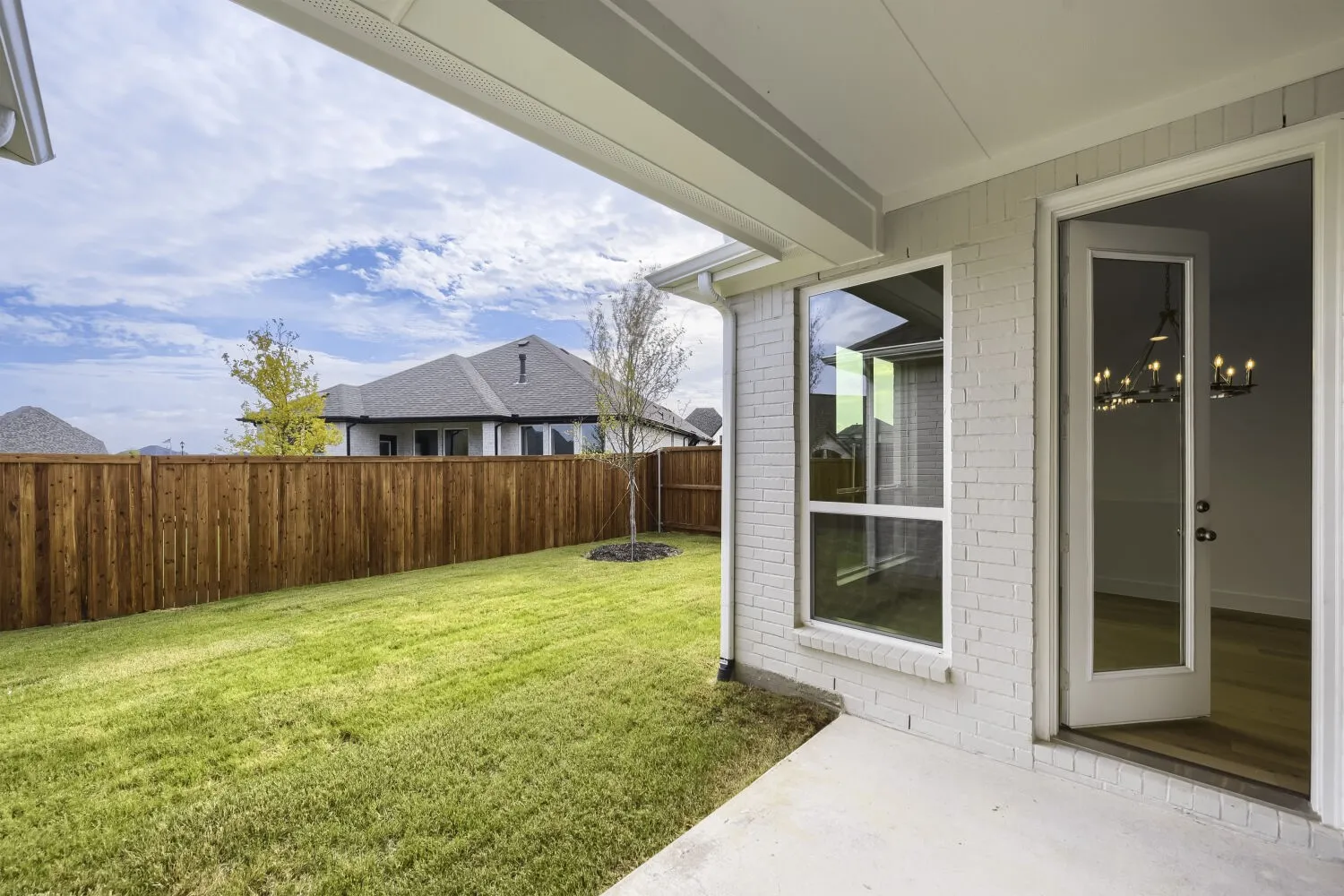 Expansive backyard featuring a manicured lawn, wood privacy fence, and concrete patio