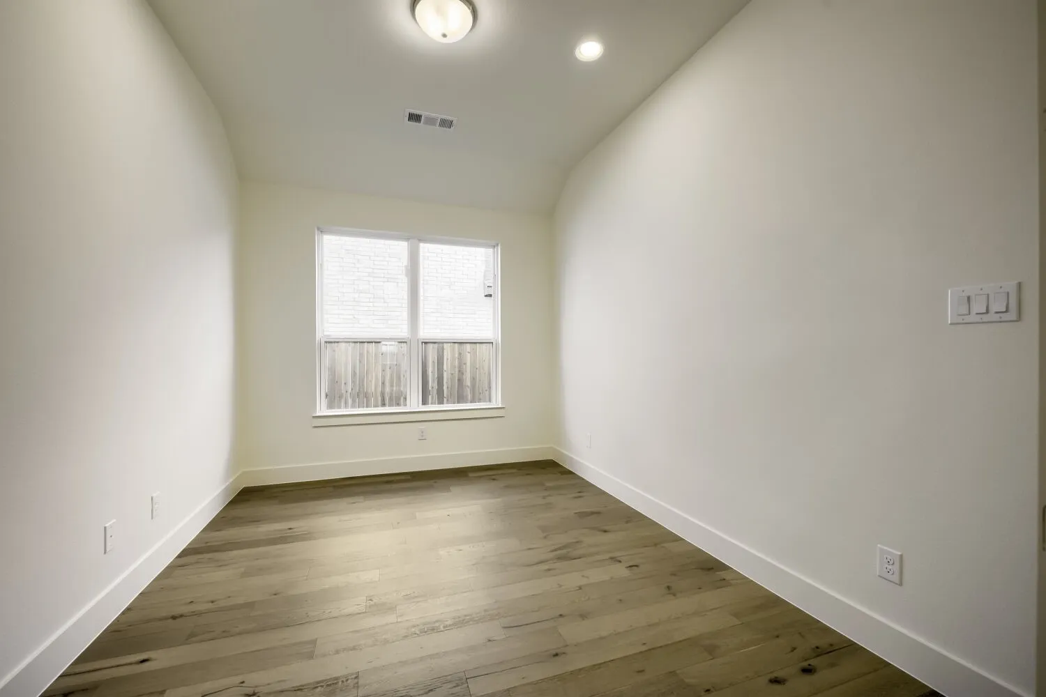 Wood-finish flooring, recessed lighting, and a flush mount ceiling fixture illuminate this space with a single window