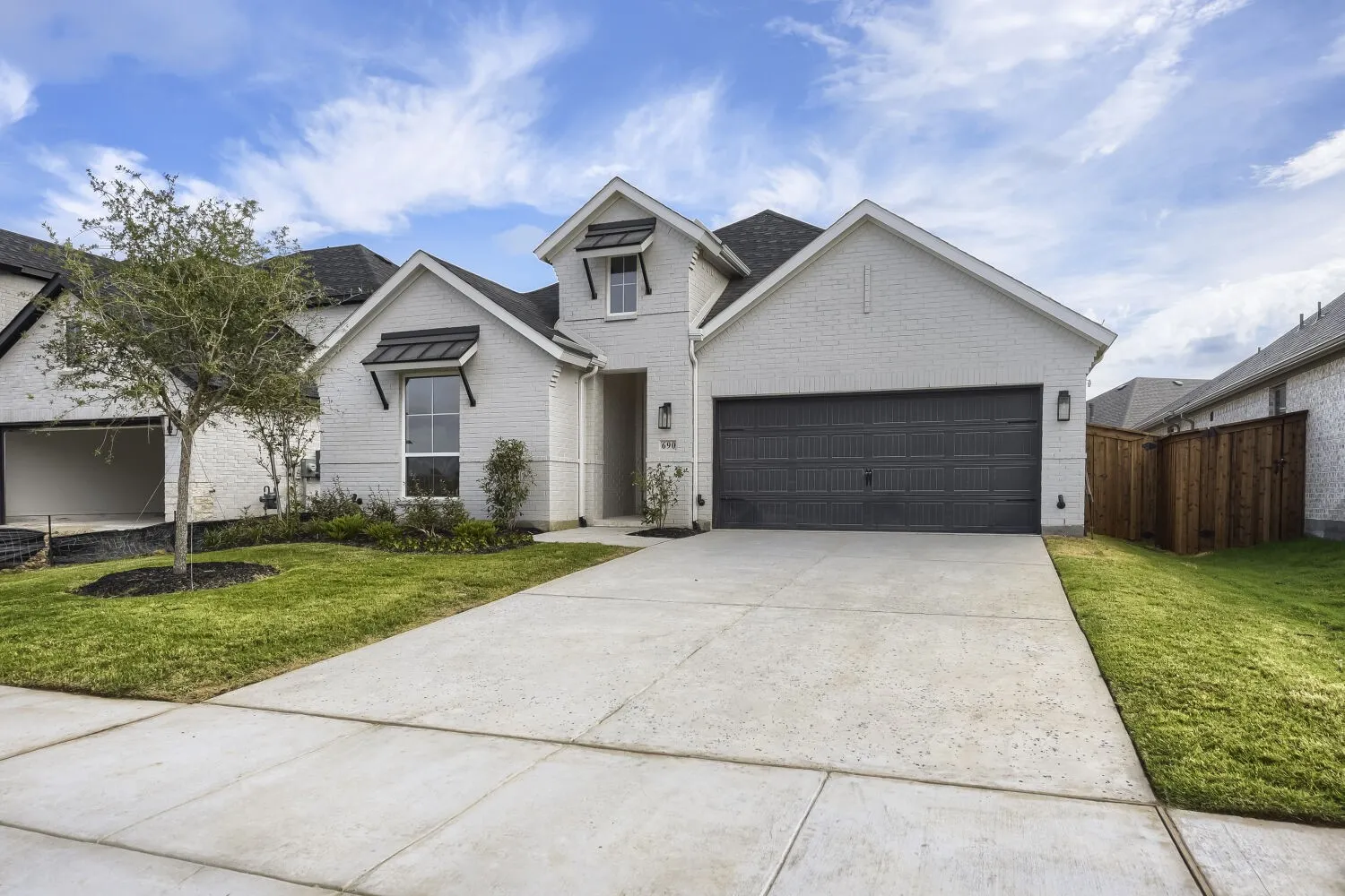 White brick exterior with dark trim accents, a two-car garage, concrete driveway, and established landscaping