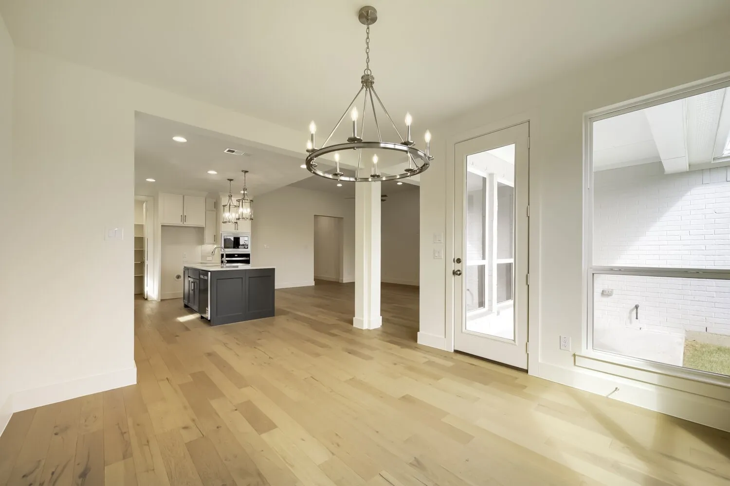 Light wood-finish flooring with a modern chandelier, white trim, and a glass-paneled door
