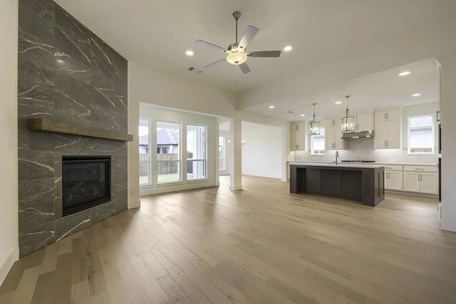 Spacious interior featuring wood-finish flooring, a contemporary fireplace with a wood mantle, and a kitchen island with pendant lighting