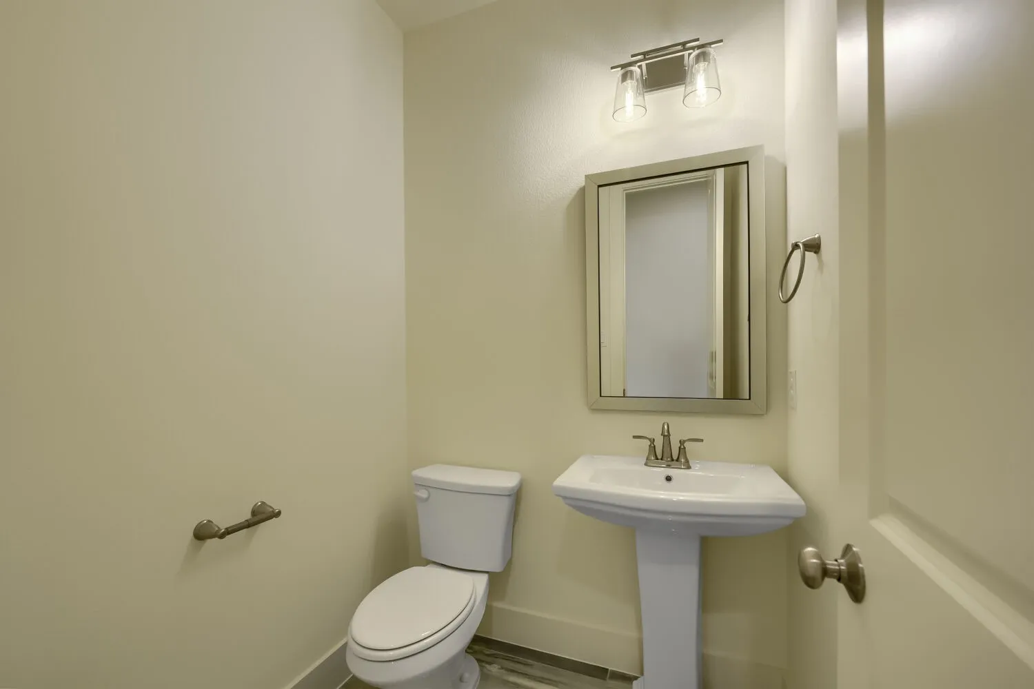 Pedestal sink with chrome faucet, wall-mounted mirror, and overhead vanity lighting