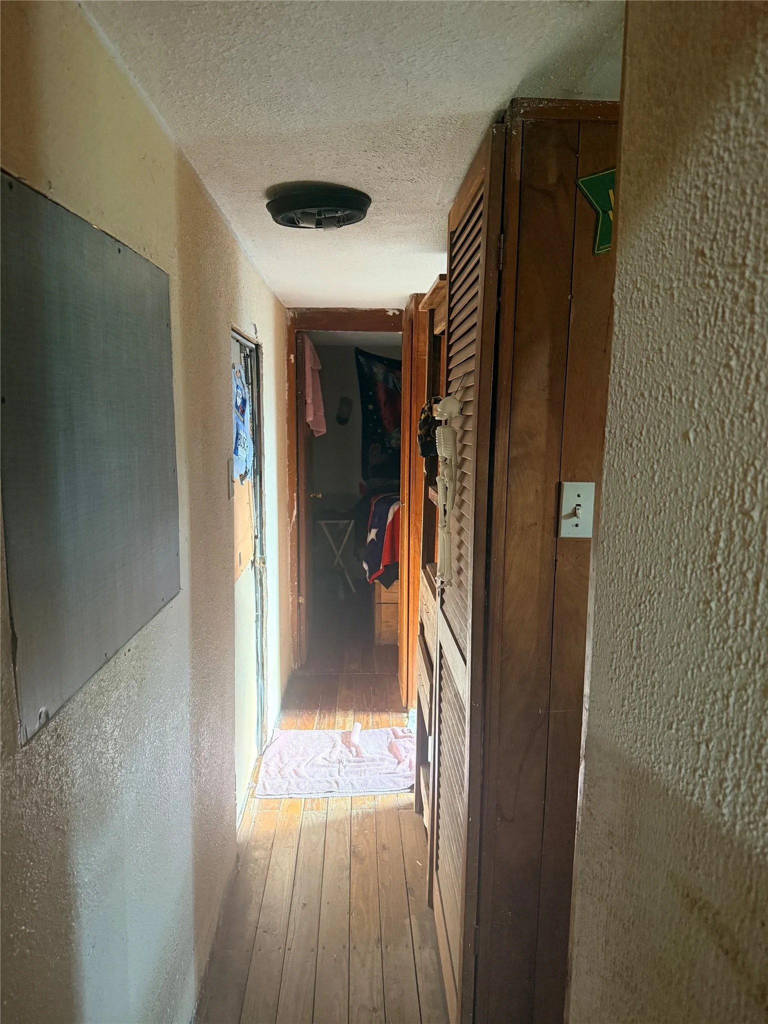 Hallway featuring wood-finish flooring, textured wall surfaces, recessed ceiling lighting, and wood-frame doorways with natural illumination from entry point