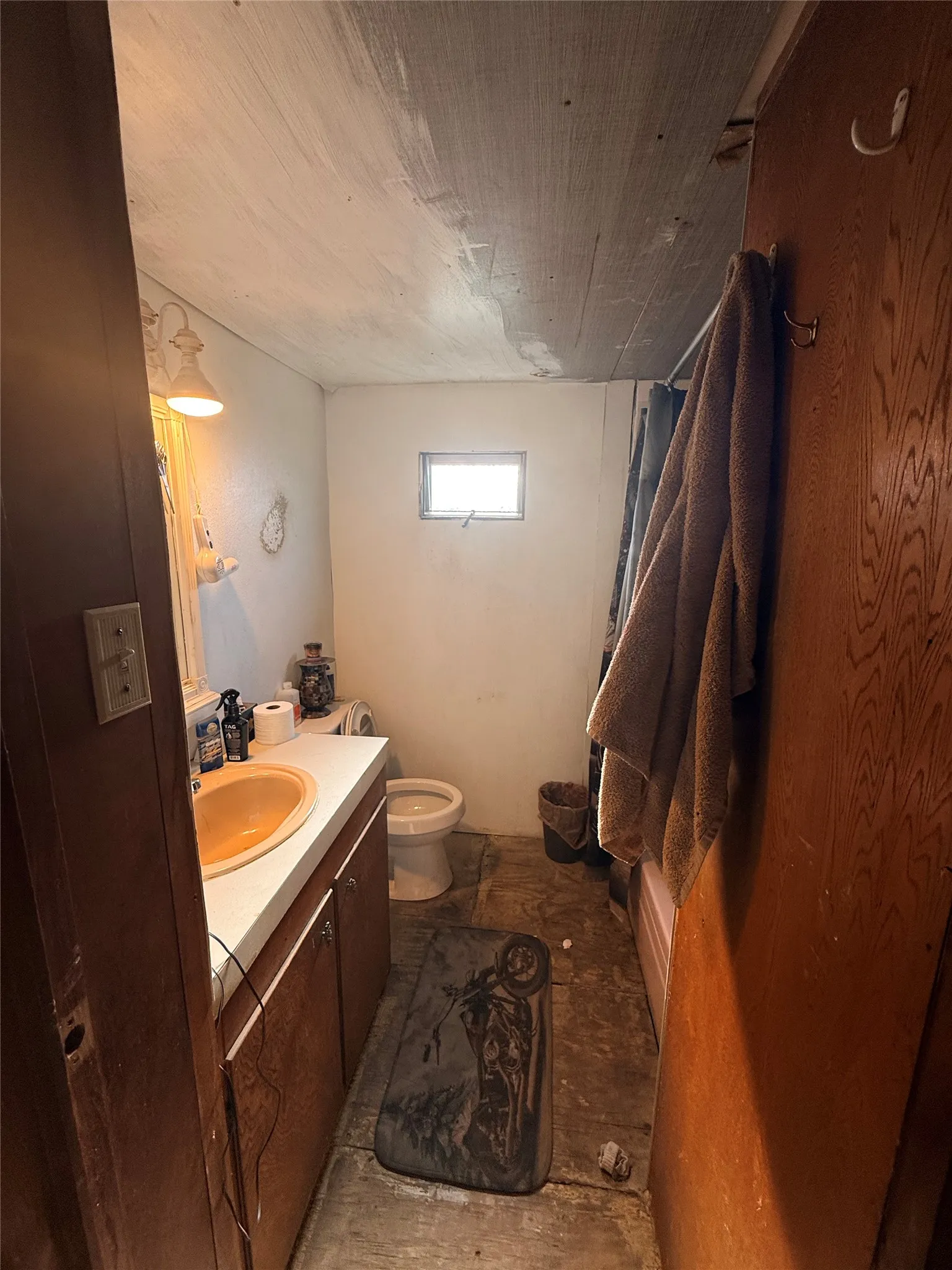 Compact bathroom featuring a ceramic sink with vanity cabinetry, toilet, and window for natural light