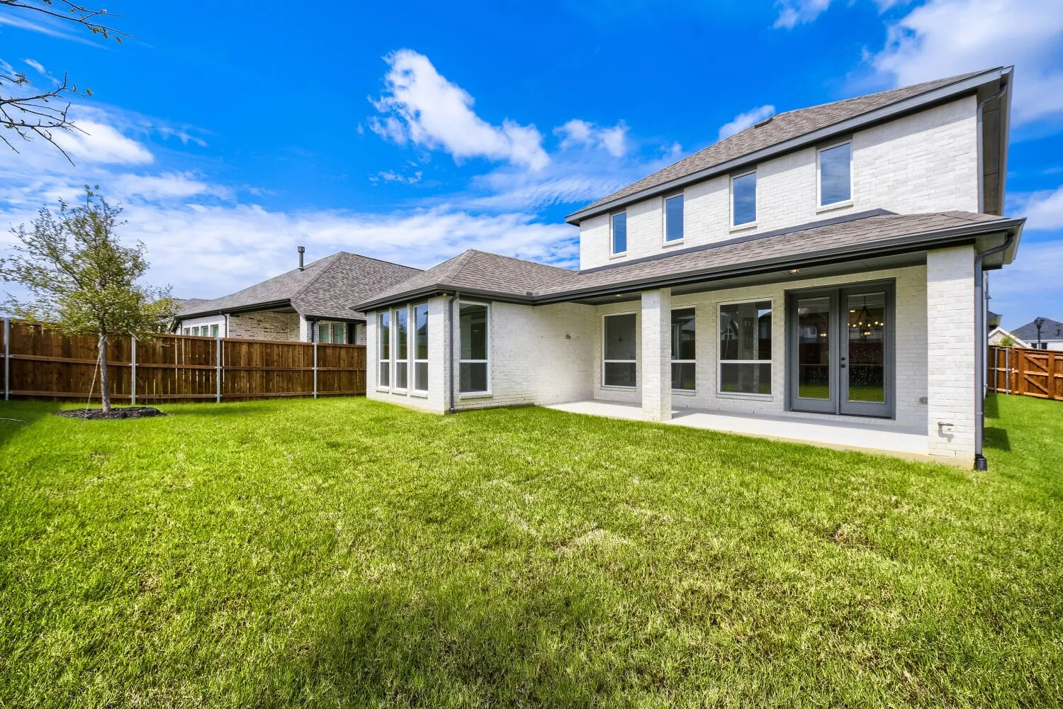 Expansive lawn featuring a newly planted tree, a covered patio, and a privacy fence