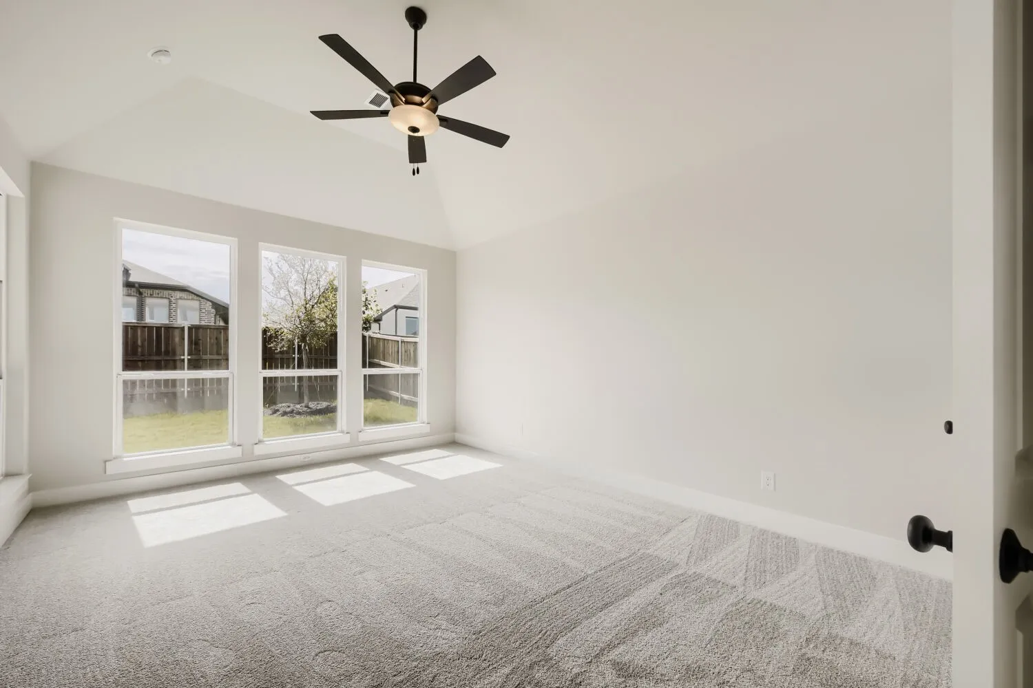 Vaulted ceiling with a contemporary ceiling fan, triple windows, and light-toned patterned carpeting