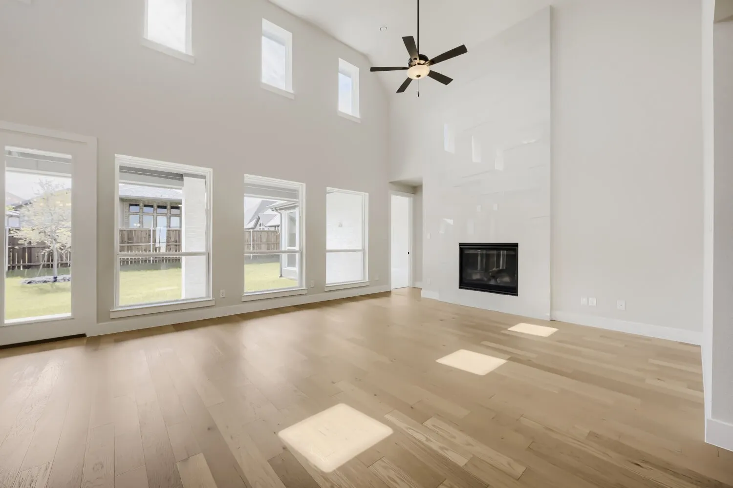 Vaulted ceilings with a ceiling fan, a fireplace with a light-colored surround, wood-finish flooring, and multiple large windows