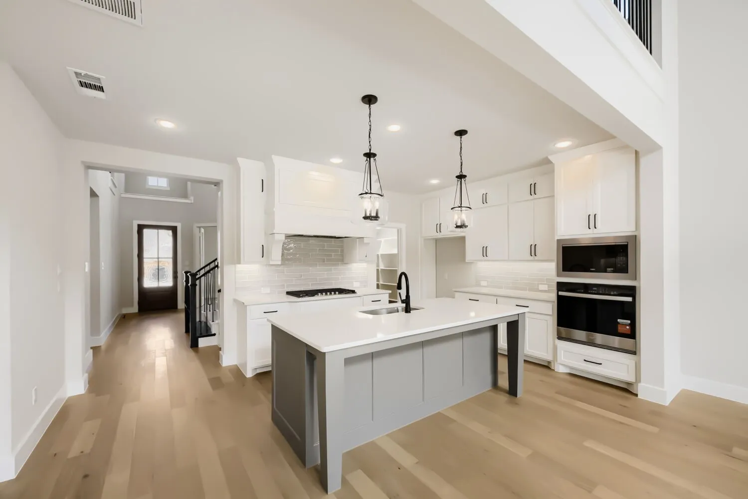 Open-concept kitchen featuring a large central island, white cabinetry, integrated stainless steel appliances, and wood-finish flooring