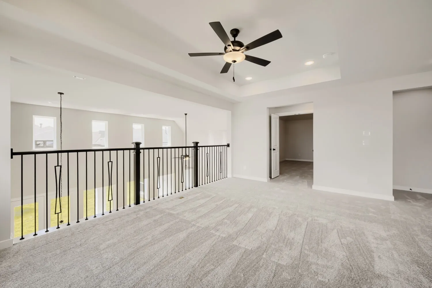 Expansive open-concept room featuring light-toned carpet, a contemporary black metal baluster railing, and a tray ceiling with recessed lighting