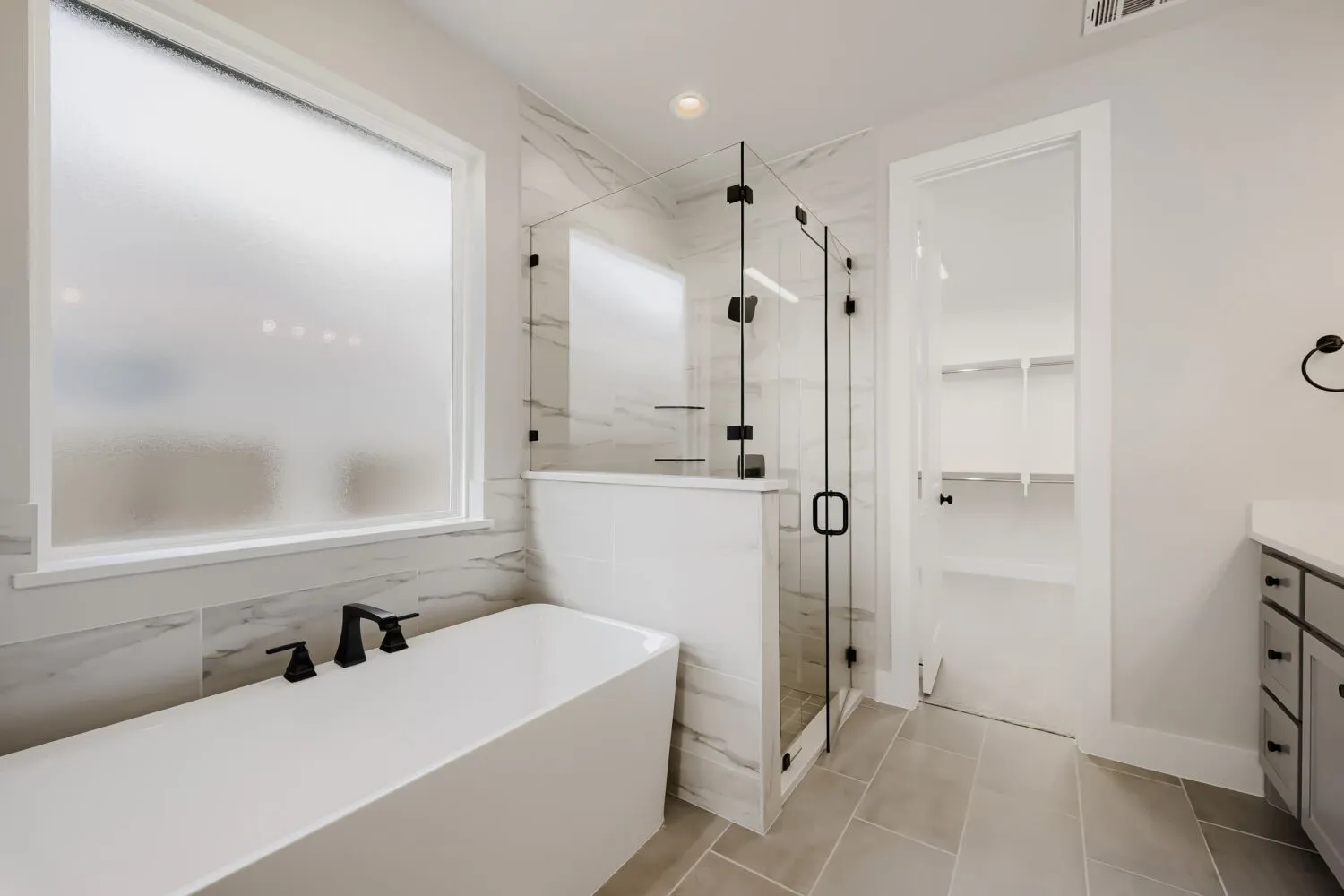 Freestanding soaking tub with matte black fixtures, framed glass shower, marble-finish wall tile, and light-toned floor tile