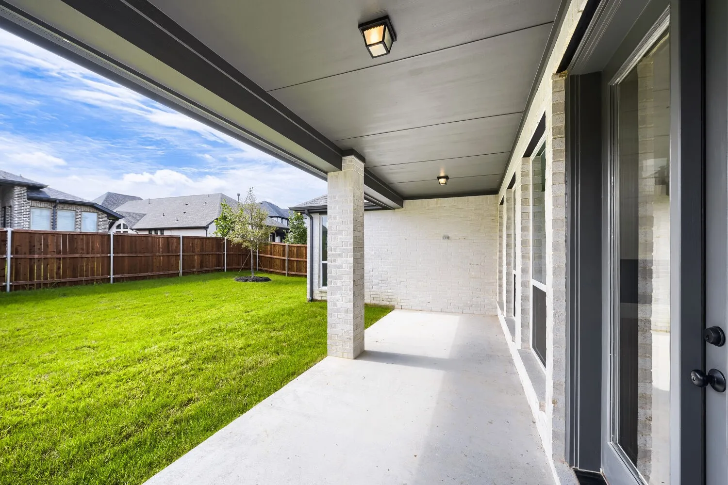 Covered concrete patio with white brick exterior, multiple windows, and a green lawn