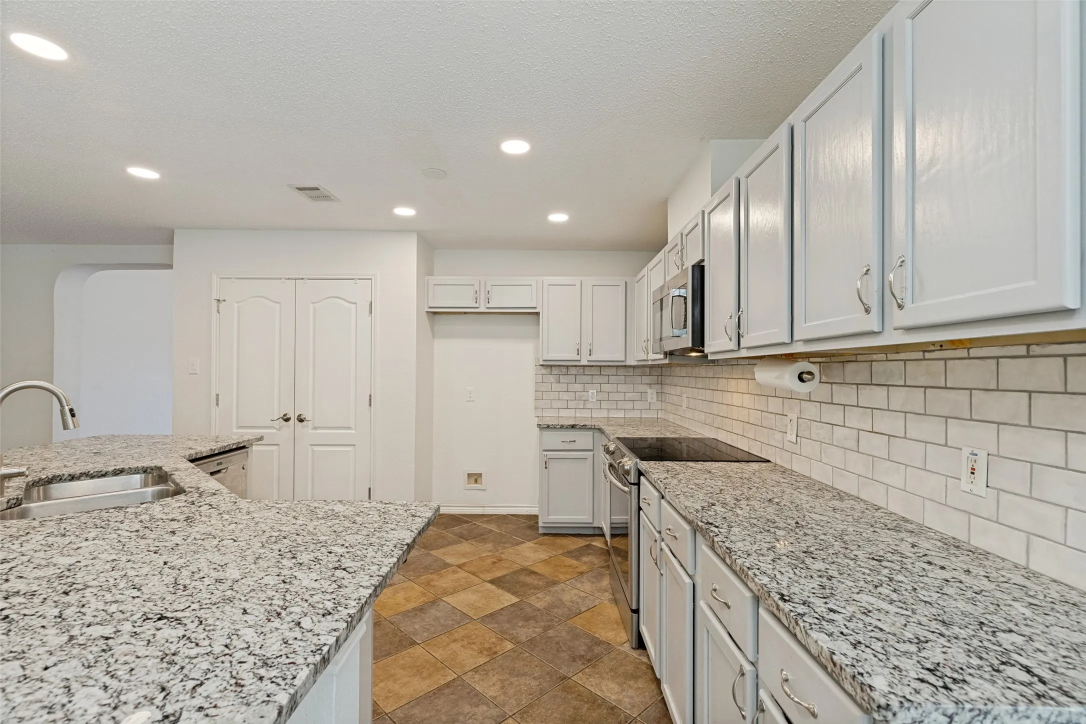Kitchen featuring granite countertops, a stainless steel sink, white cabinetry, subway tile backsplash, and recessed lighting