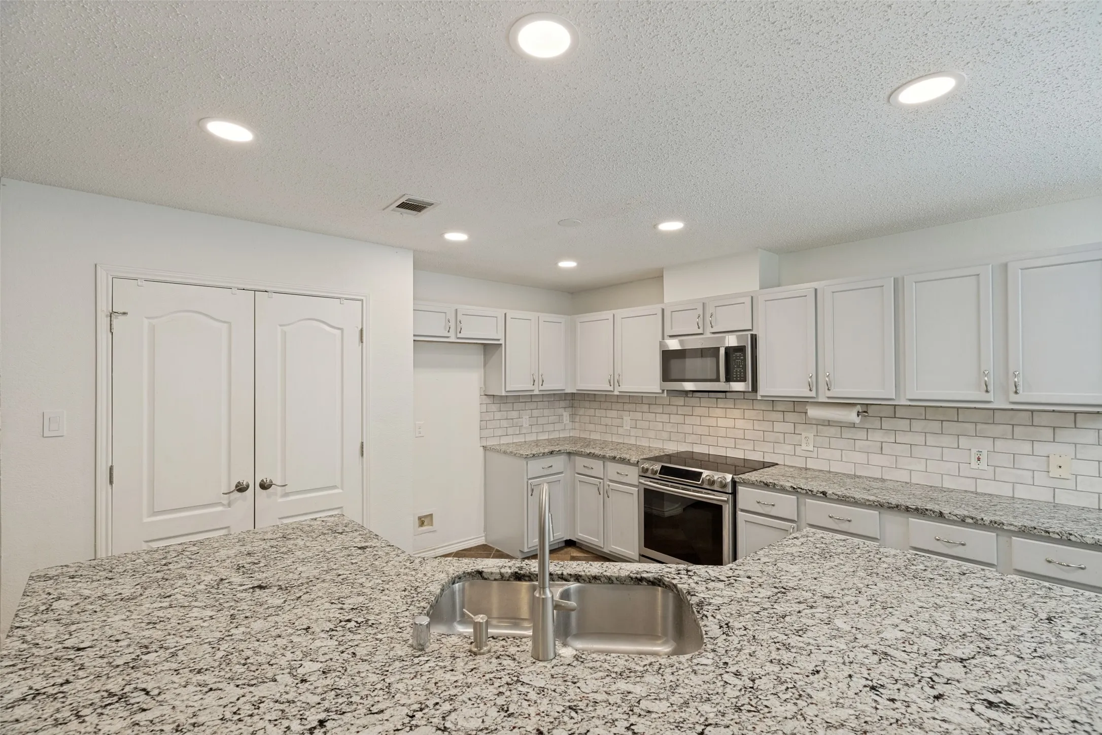 Kitchen featuring recessed lighting, light-toned cabinetry, stainless steel appliances, subway tile backsplash, and a large island with an undermount sink