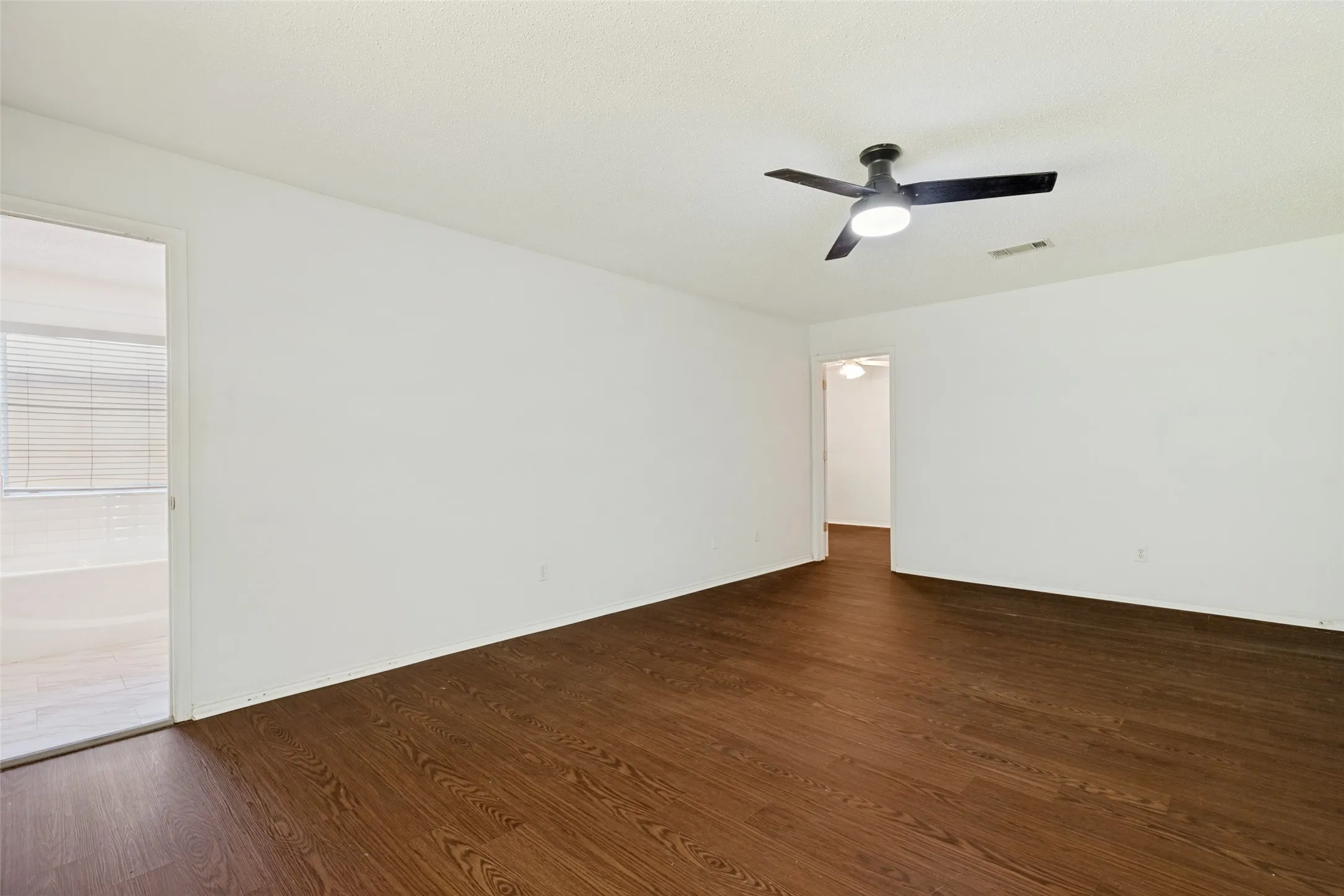 Expansive interior space featuring wood-finish flooring, white walls, and a ceiling fan with integrated lighting