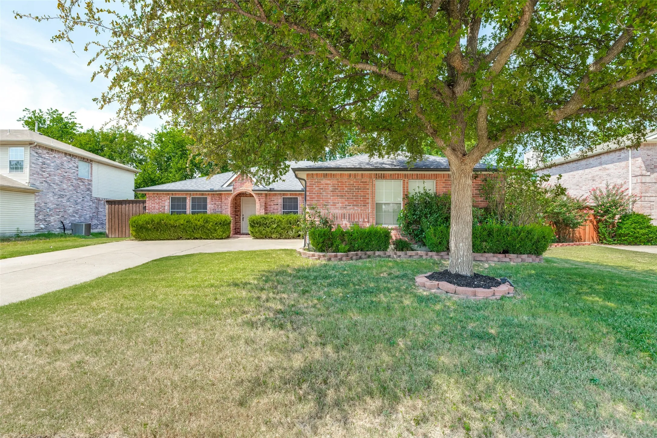 Brick exterior with an arched entryway, established landscaping, and a concrete driveway