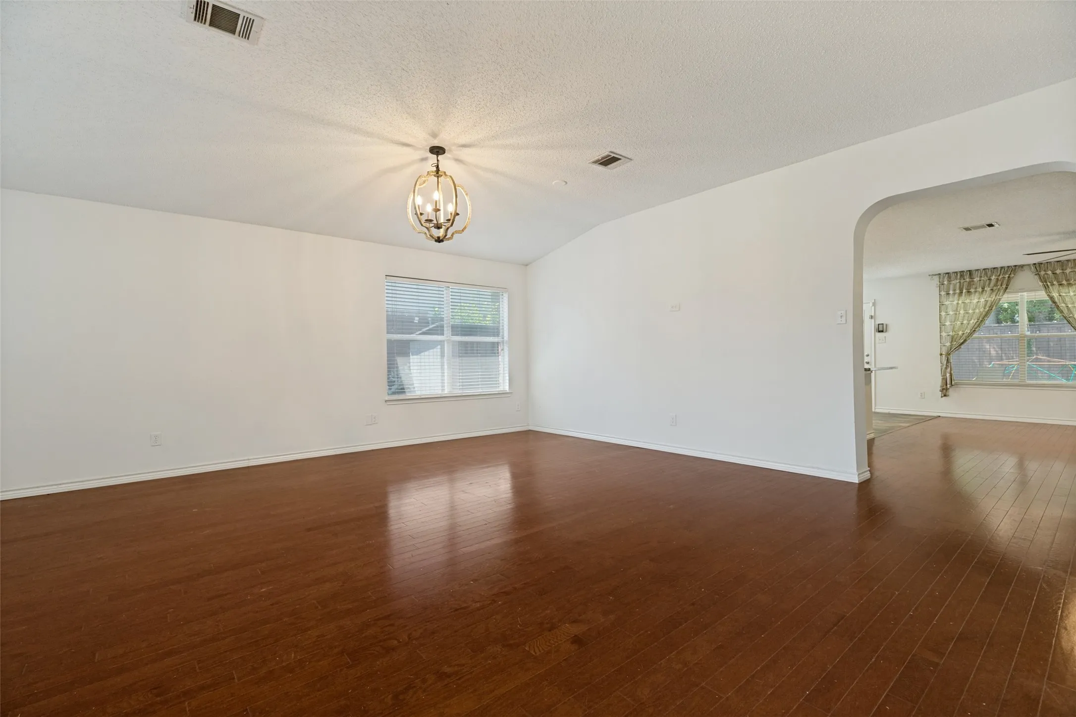 Vaulted ceiling with an ornate chandelier, wood-finish flooring, and an arched doorway