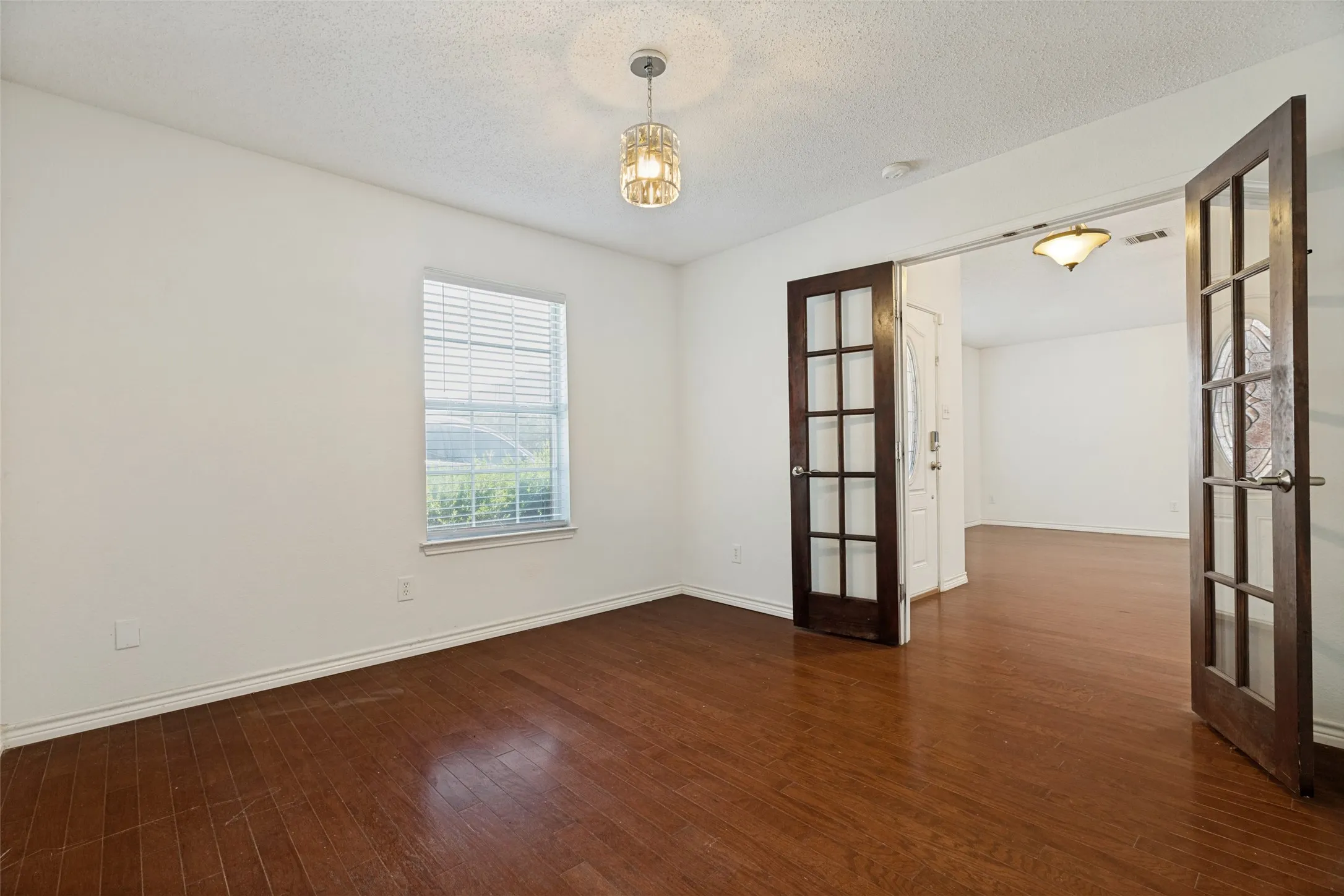 Hardwood-finish flooring, white walls, double French doors, and a decorative ceiling light fixture