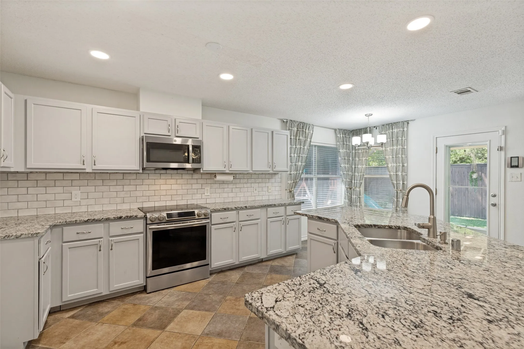 Kitchen featuring white shaker-style cabinetry, stainless steel appliances, granite countertops, subway tile backsplash, and recessed lighting