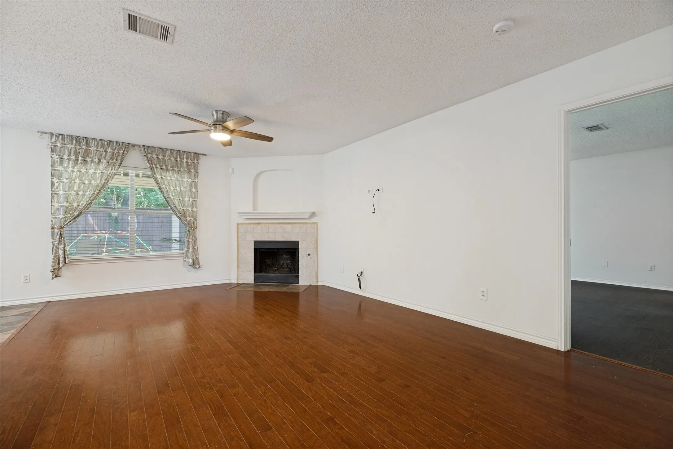 Hardwood-finish flooring, recessed fireplace with a stone surround, ceiling fan with integrated lighting, and white walls