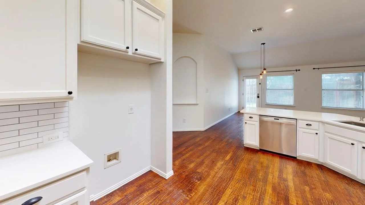 Spacious kitchen featuring white cabinetry with stainless steel appliances, subway tile backsplash, quartz countertops, and warm wood-finish flooring throughout