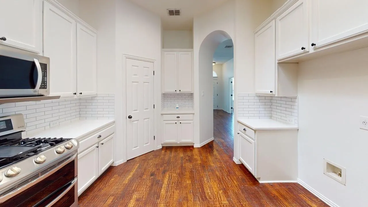 Kitchen featuring wood-finish flooring, white cabinetry with black hardware, and subway tile backsplash