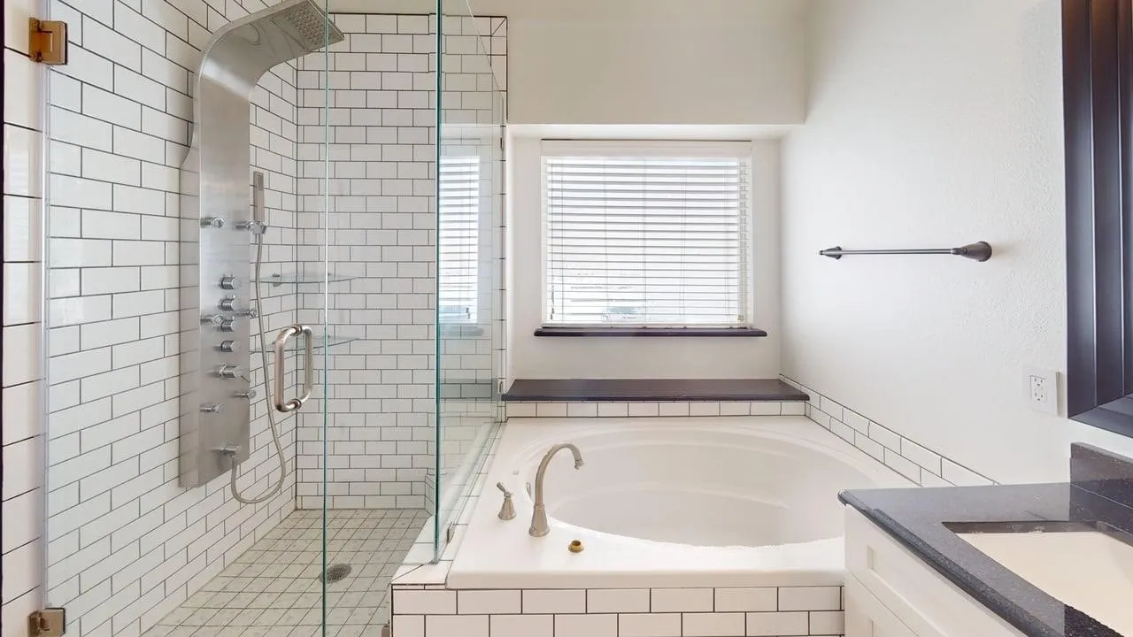 Spa-inspired primary bathroom featuring a frameless glass-enclosed walk-in shower with subway tile surround, a deep soaking tub positioned beneath a transom window, polished chrome fixtures, and heated tile flooring throughout