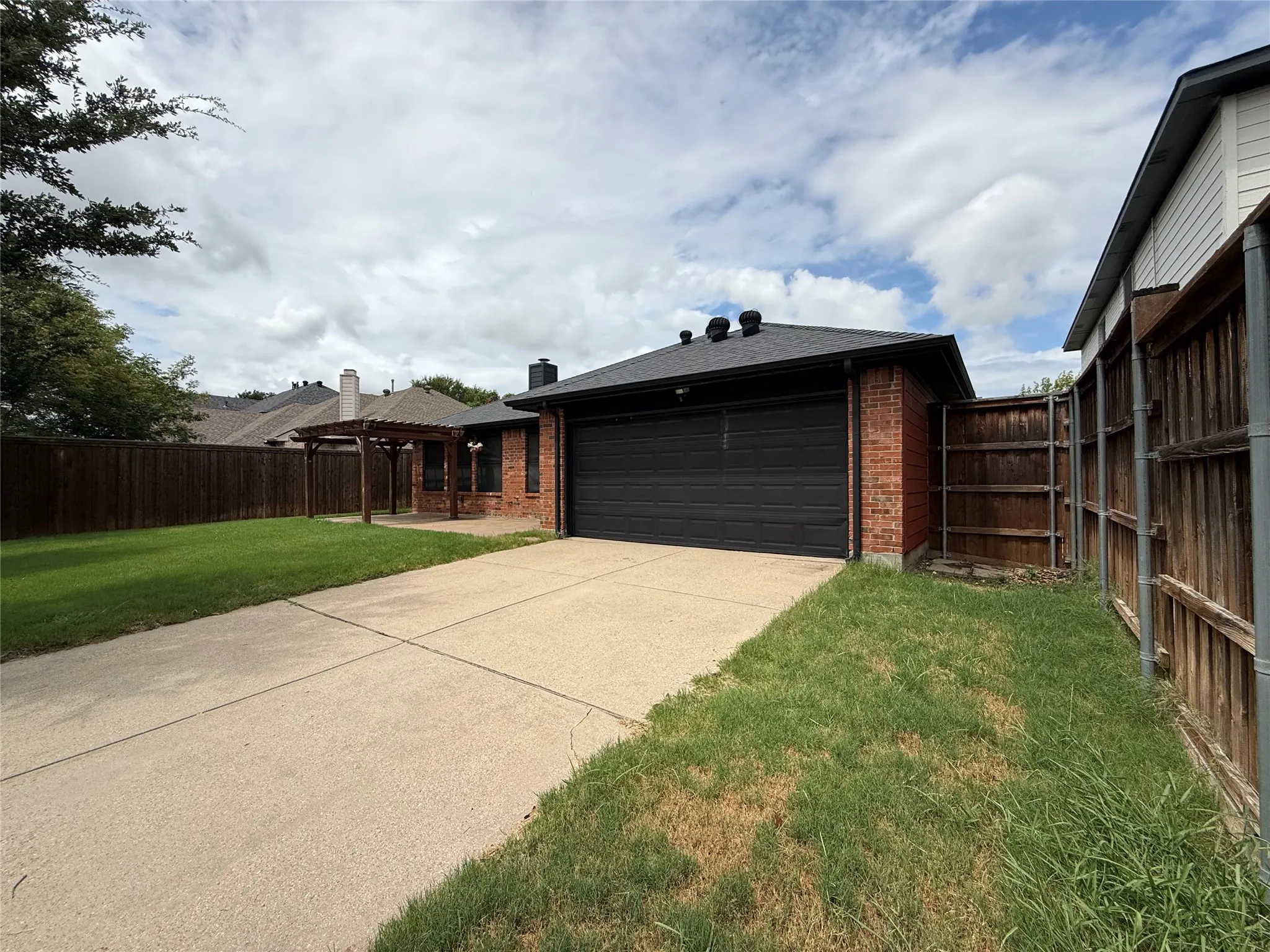 Brick exterior featuring a dark garage door, concrete driveway, and wooden privacy fencing
