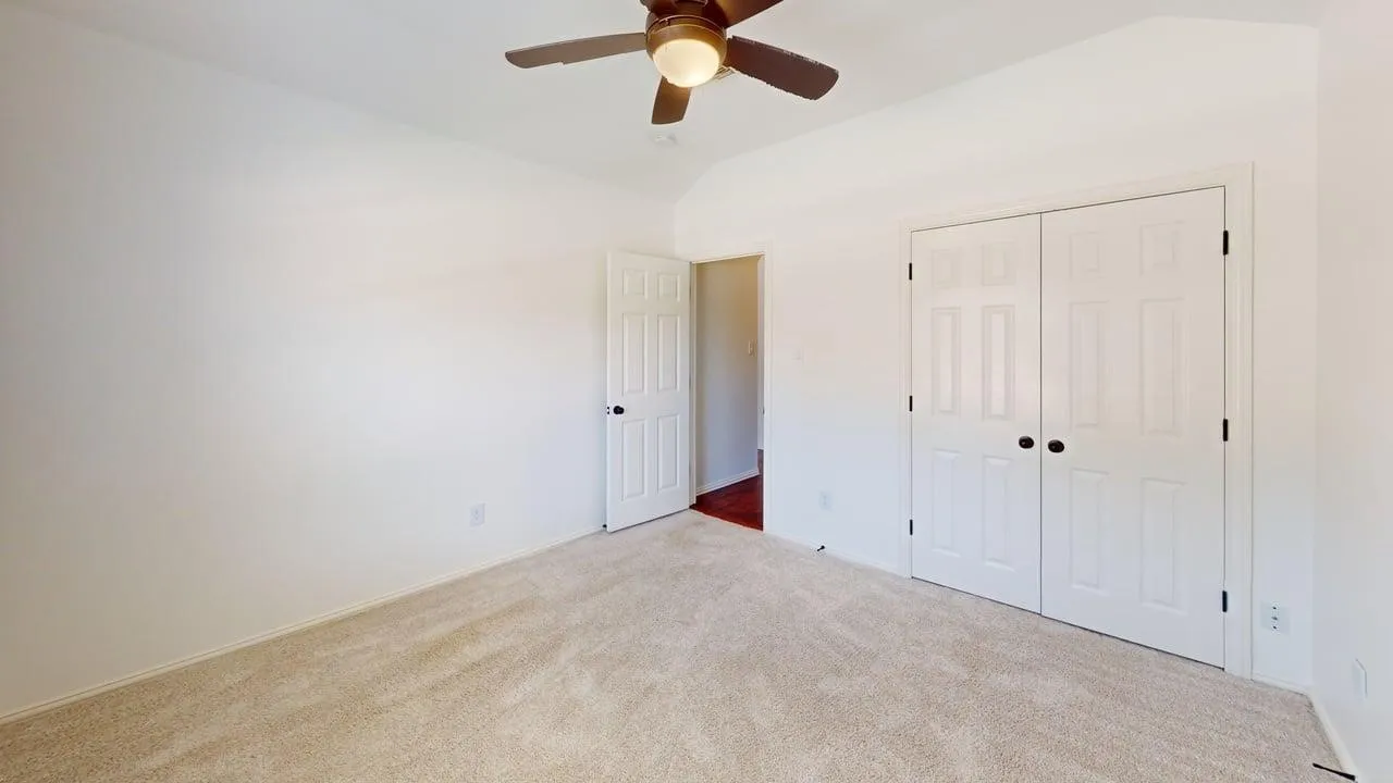 Spacious bedroom featuring neutral carpeting, a ceiling fan with integrated lighting, and dual closet storage with white panel doors
