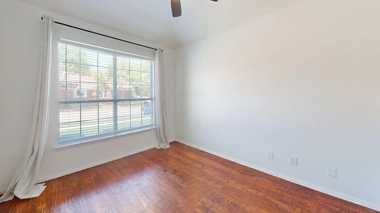 Spacious room featuring wood-finish flooring, white walls, and a large window with horizontal blinds