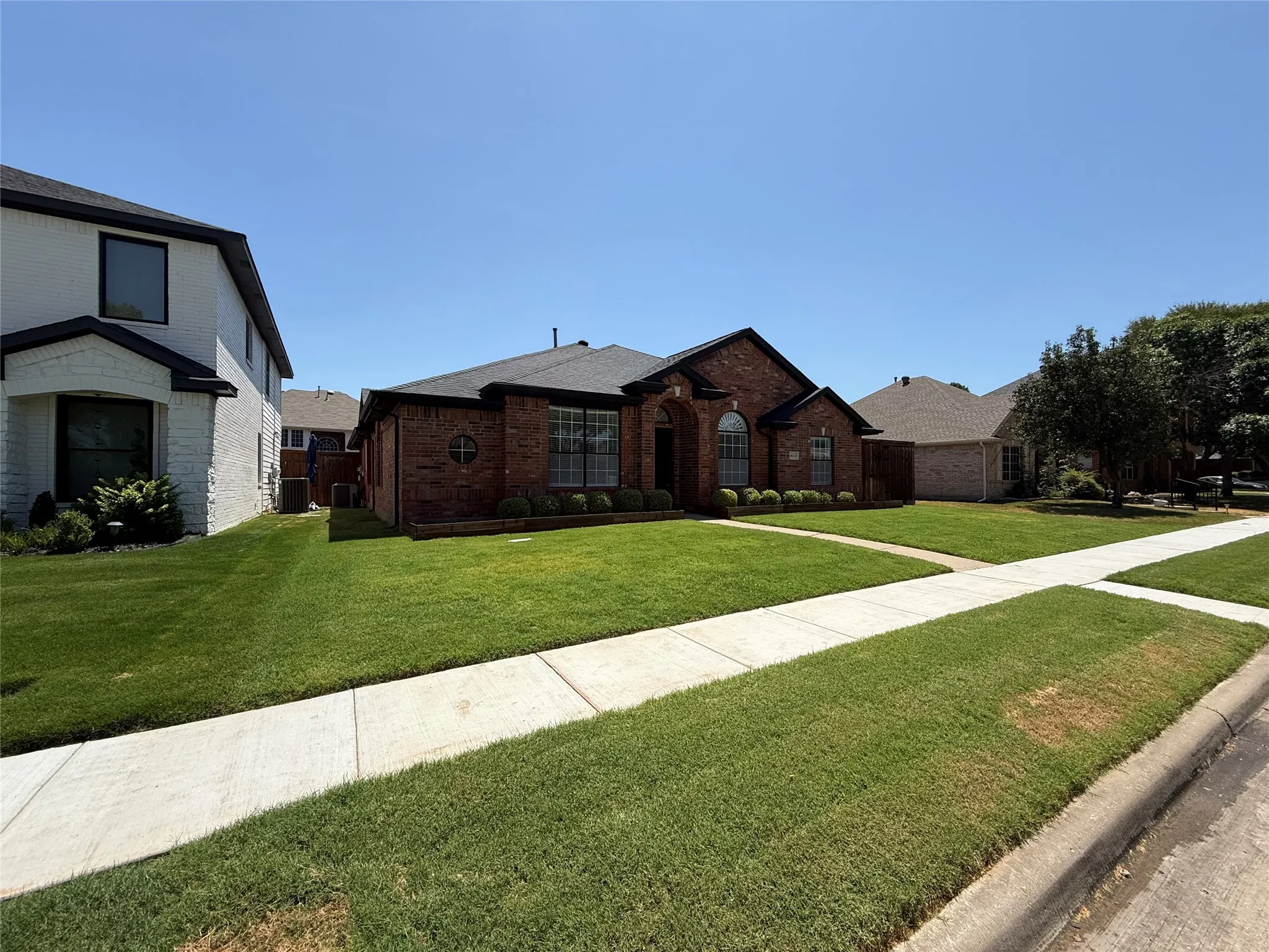 Charming brick residence showcasing a sprawling manicured lawn, concrete walkway, and mature landscaping