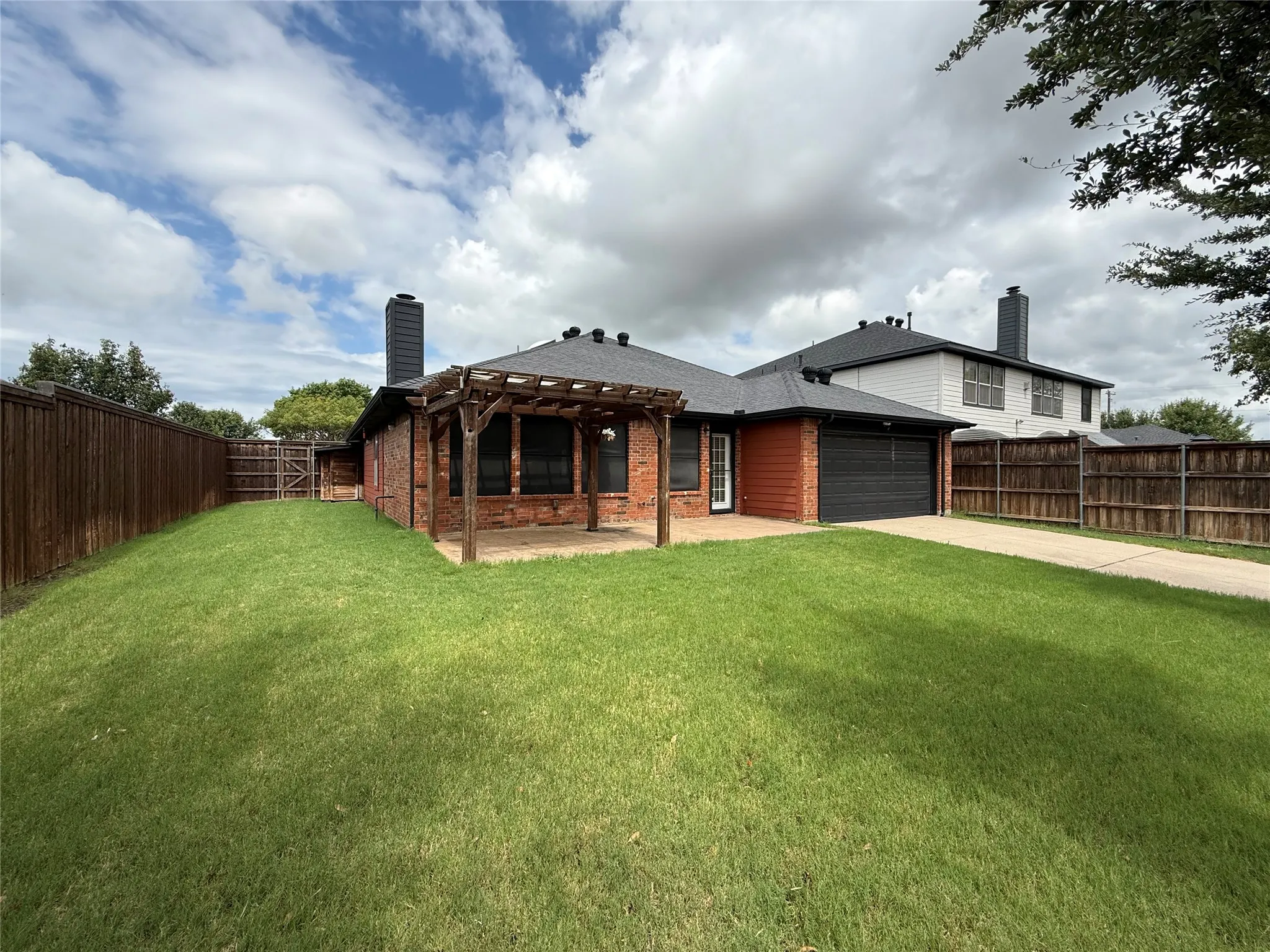 Expansive backyard featuring a manicured lawn bordered by timber fencing, with a brick-constructed covered pavilion offering sheltered outdoor space