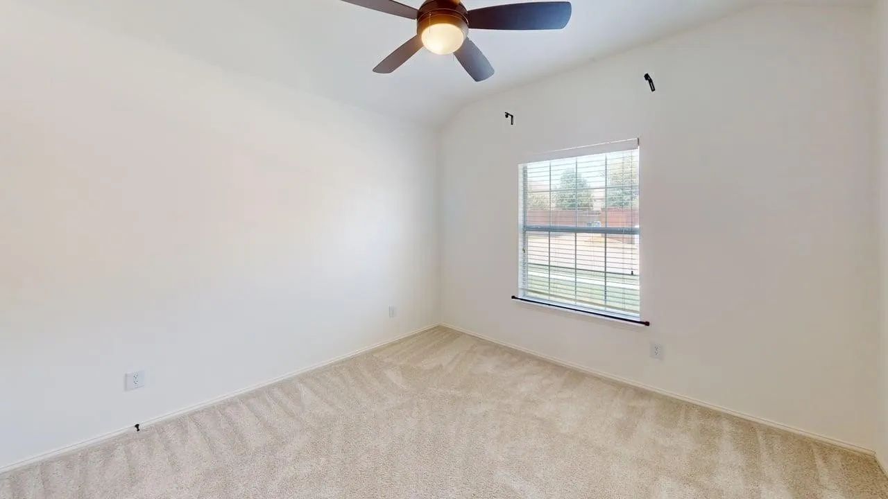 Bright bedroom featuring neutral carpet flooring, a ceiling fan with integrated light fixture, and a large window with horizontal blinds providing natural illumination