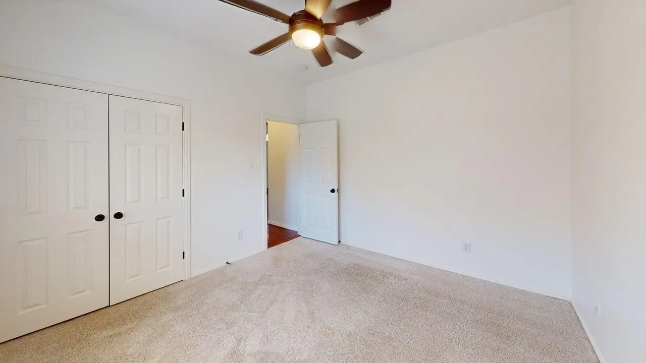 Spacious bedroom featuring neutral carpet flooring, a ceiling fan with integrated lighting, and dual closets with white six-panel doors