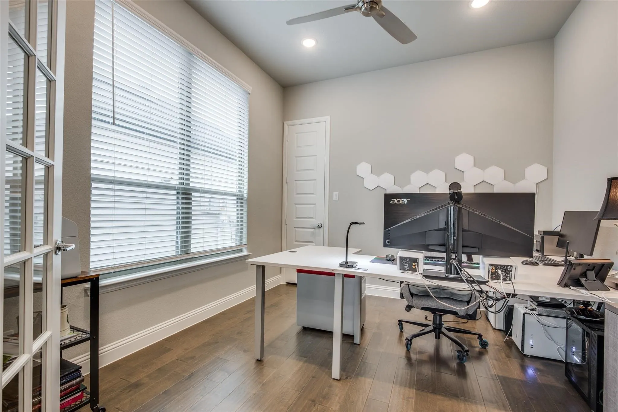 Spacious room featuring wood-finish flooring, a large window with horizontal blinds, and a vaulted ceiling with a ceiling fan