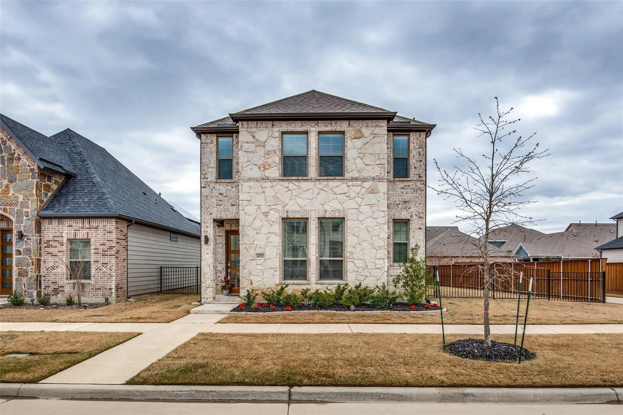 Modern two-story residence featuring a light-colored brick and stone exterior with a symmetrical façade, multiple large windows with dark frames, and a prominent peaked roofline