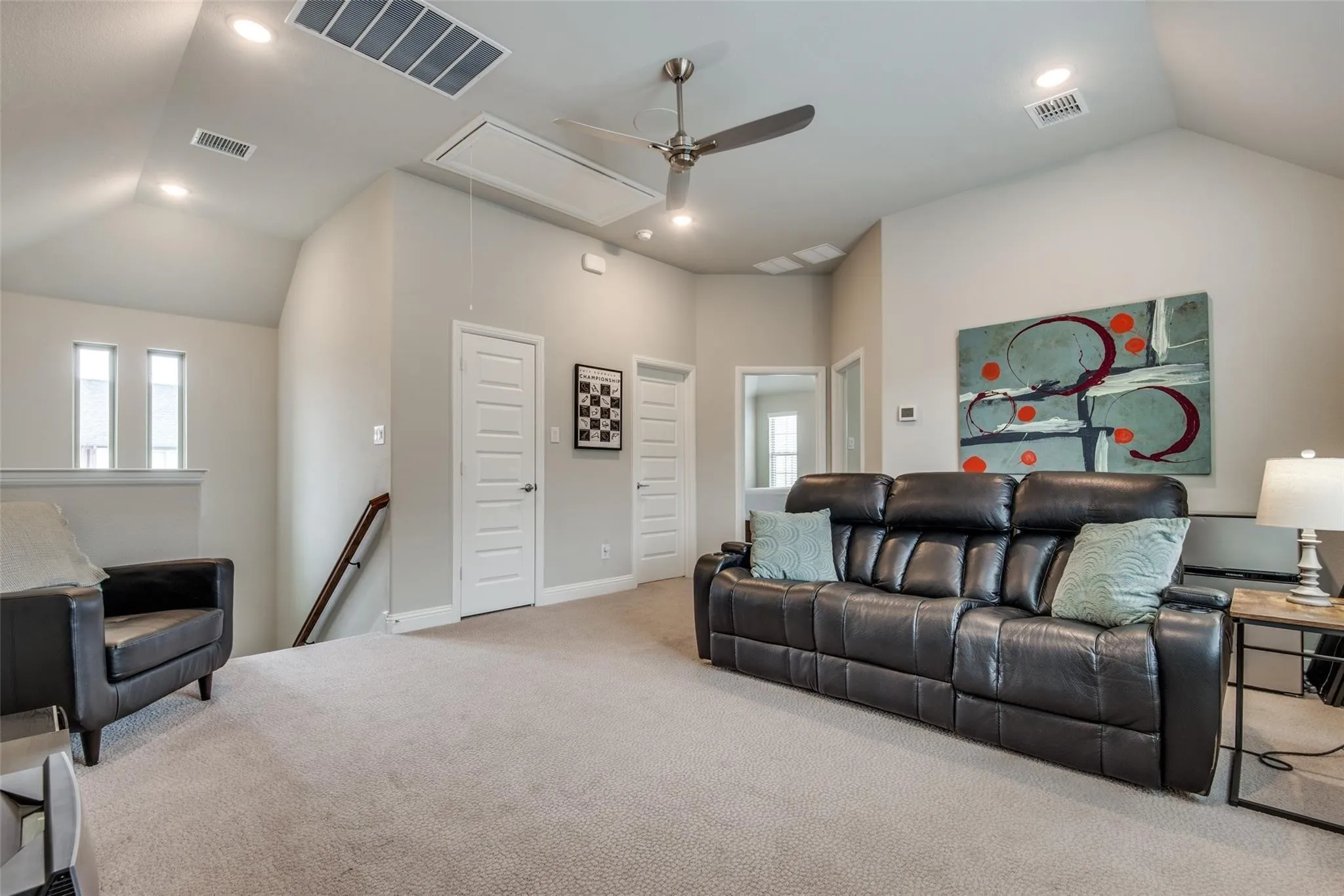 Spacious recreational room featuring soaring vaulted ceilings with recessed lighting and ceiling fan, neutral wall finishes, plush carpet flooring, and multiple white six-panel doors providing access to adjoining spaces