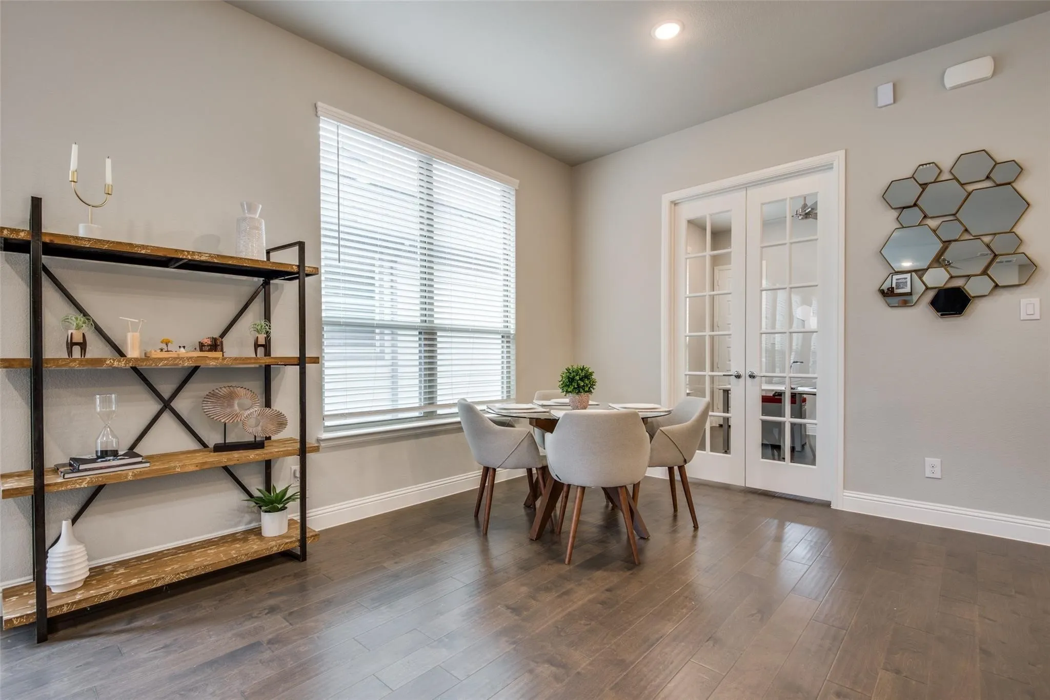 Bright, open dining area featuring hardwood flooring, large windows with plantation shutters, and a round dining table with upholstered chairs