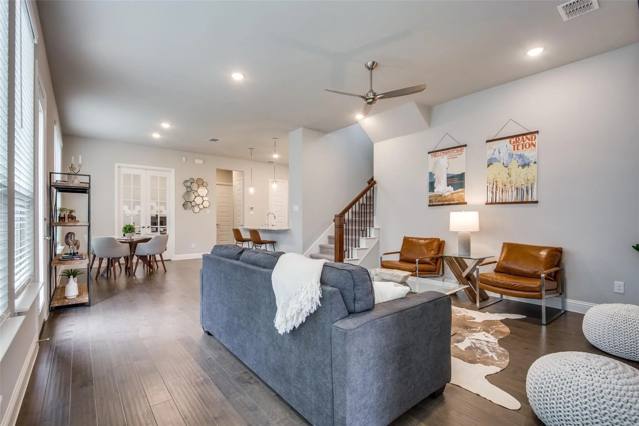 Open-concept living space anchored by a spacious gray upholstered sectional sofa, hardwood flooring throughout, and abundant natural light from expansive windows