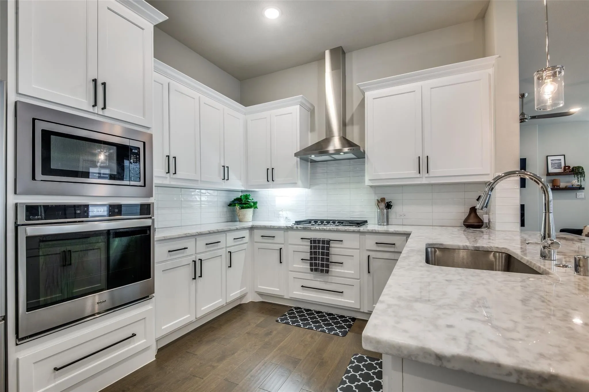 Modern kitchen featuring white cabinetry with black hardware, stainless steel appliances including a built-in oven and microwave, stone countertops, and wood-finish flooring
